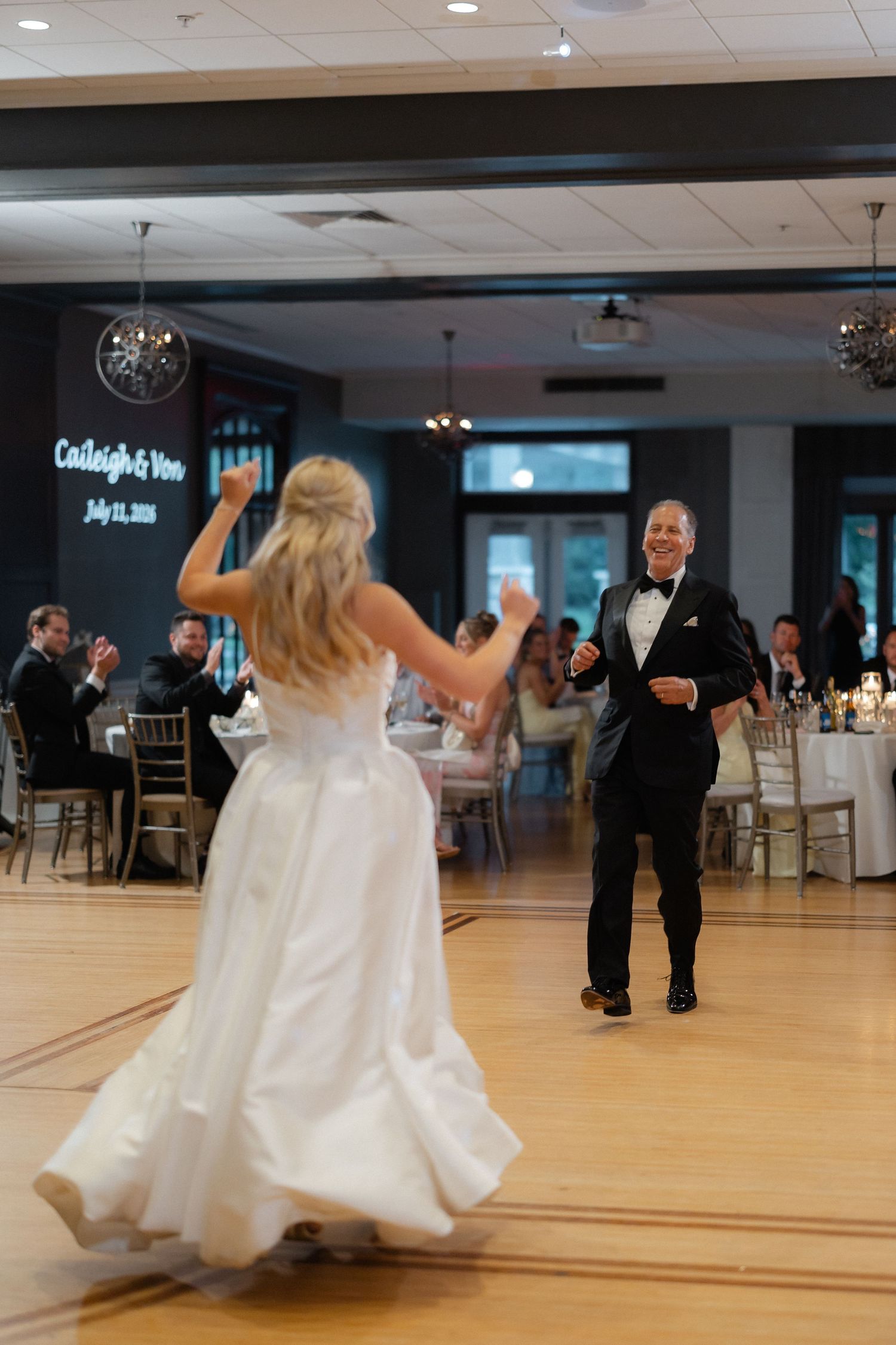 Bride and groom sharing first dance at wedding reception with names projected on wall behind them.