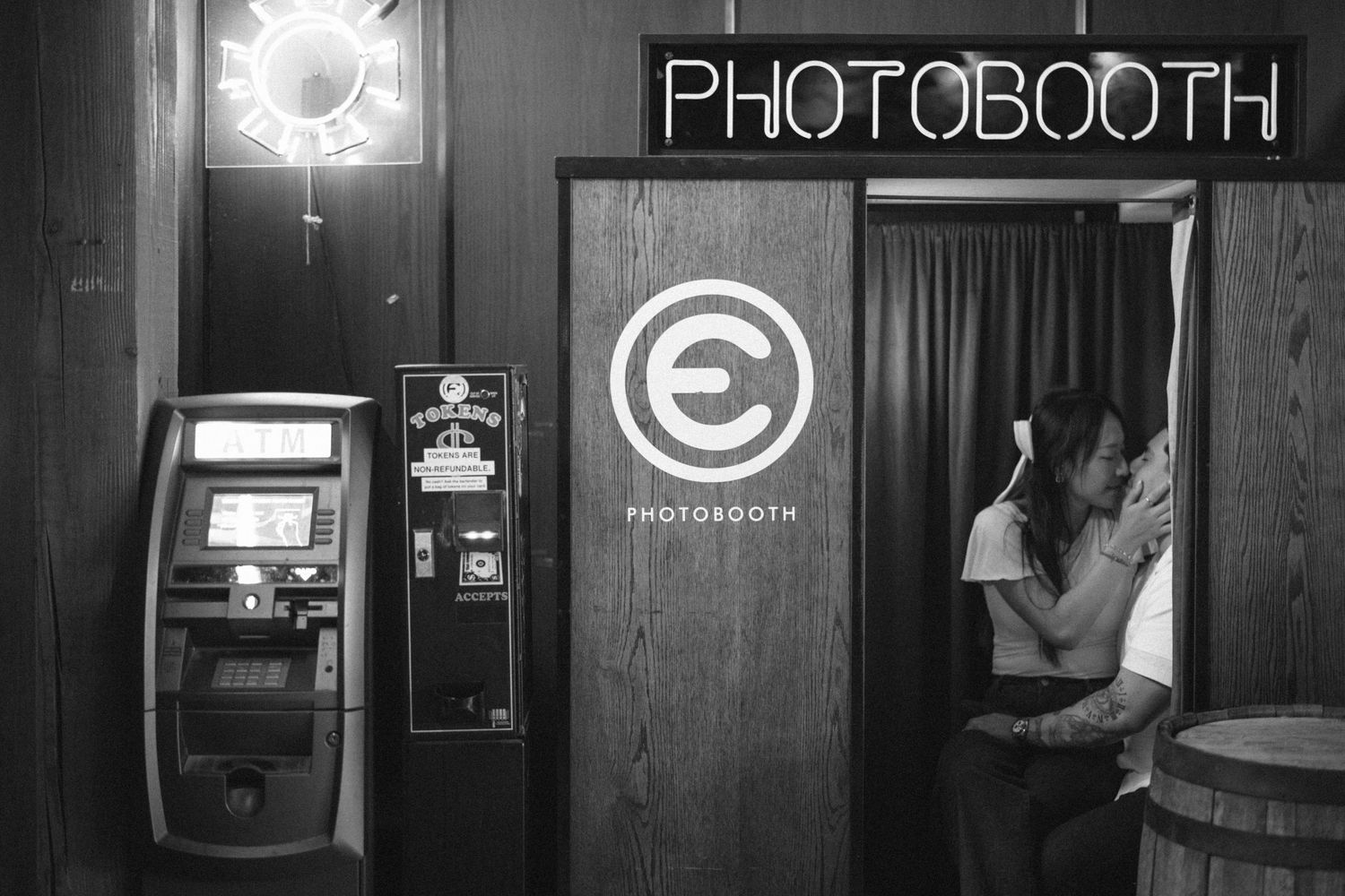 Black and white photo of a couple kissing inside a vintage photobooth at an event venue.