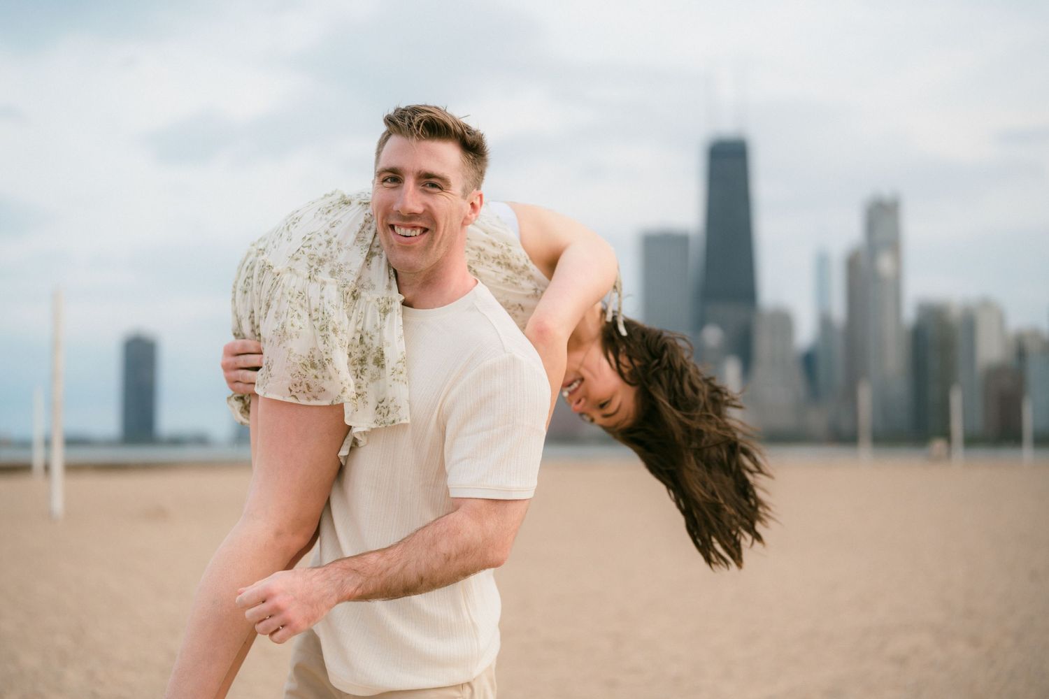 Man playfully carrying woman upside down on a Chicago beach with iconic city skyline in background.