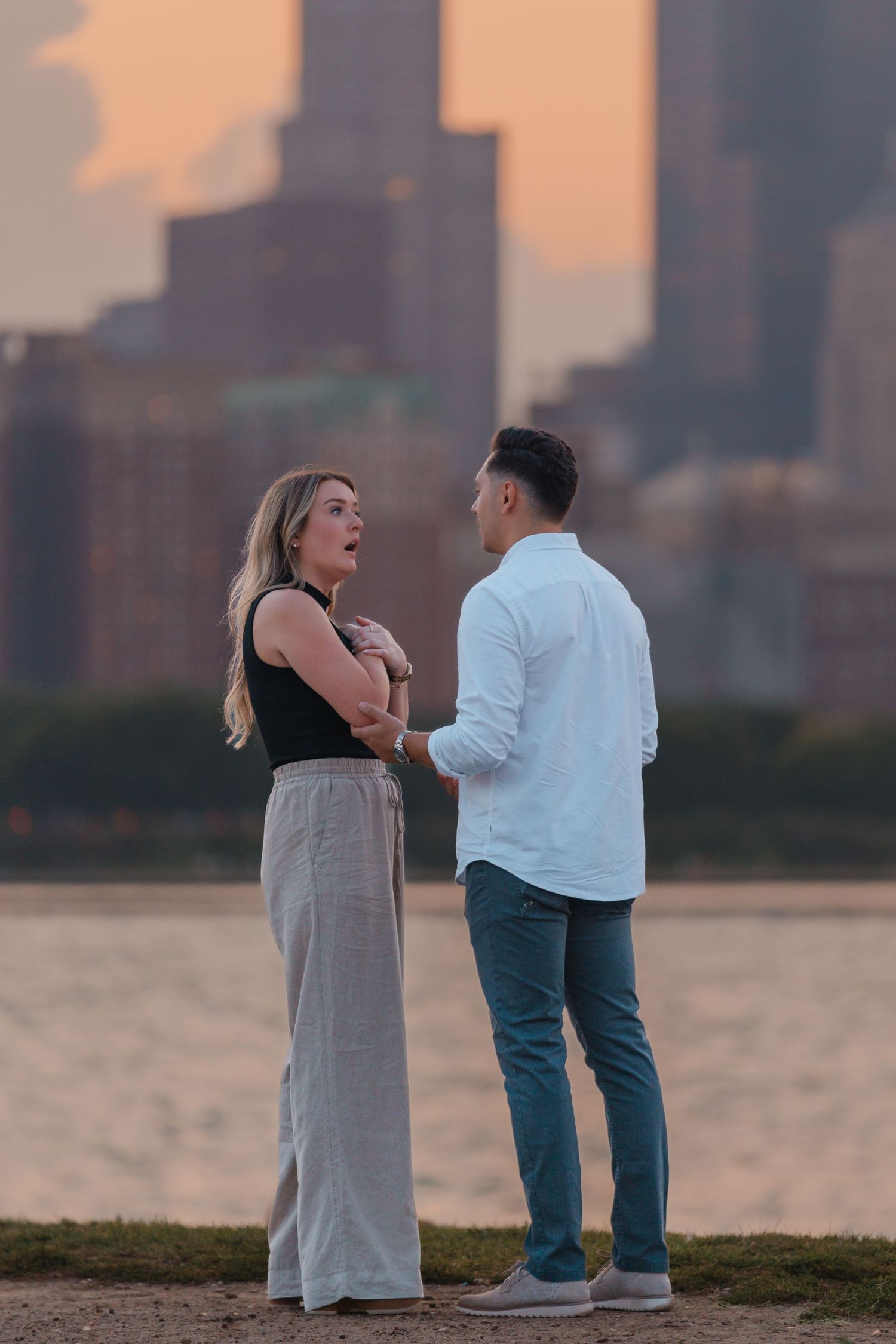 Couple holding hands and sharing a surprised moment by Lake Michigan with Chicago city skyline at sunset.