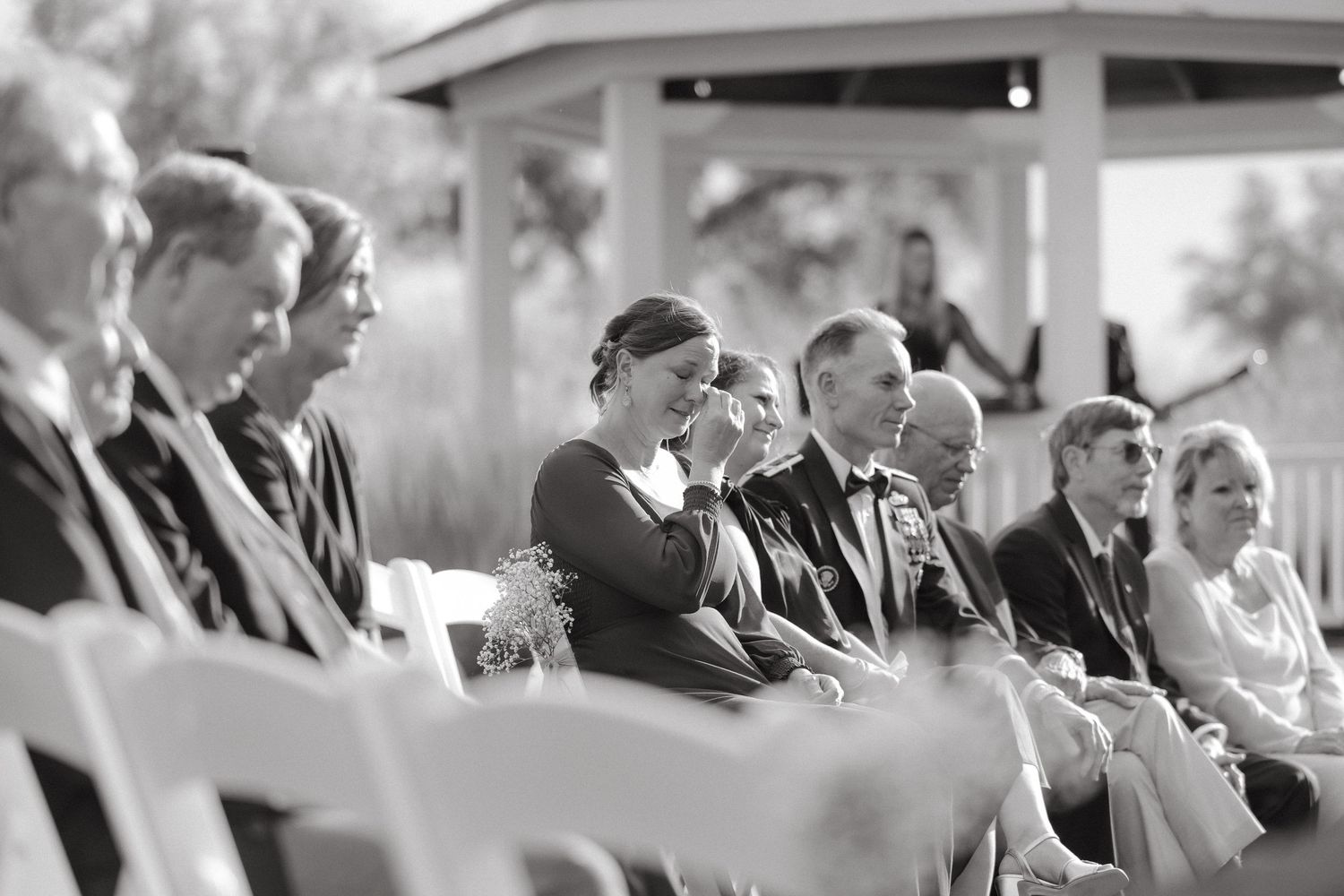 Black and white photo of emotional wedding guests seated in white chairs during outdoor ceremony.