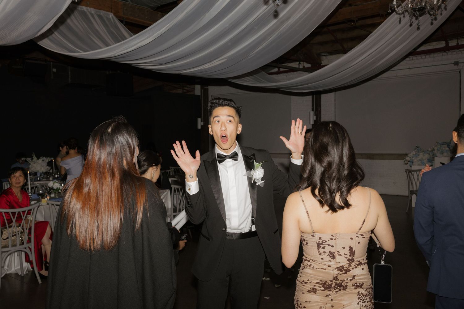 Surprised groom dances with hands raised at lively wedding reception.