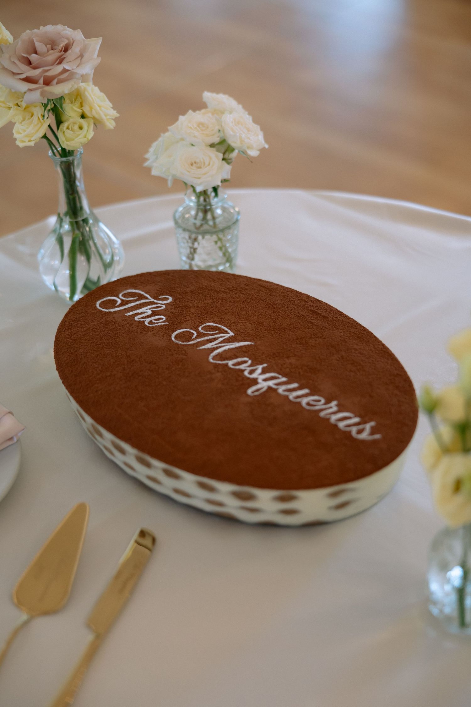 Elegant tiramisu wedding cake labeled The Mosqueras on a white tablecloth with roses.