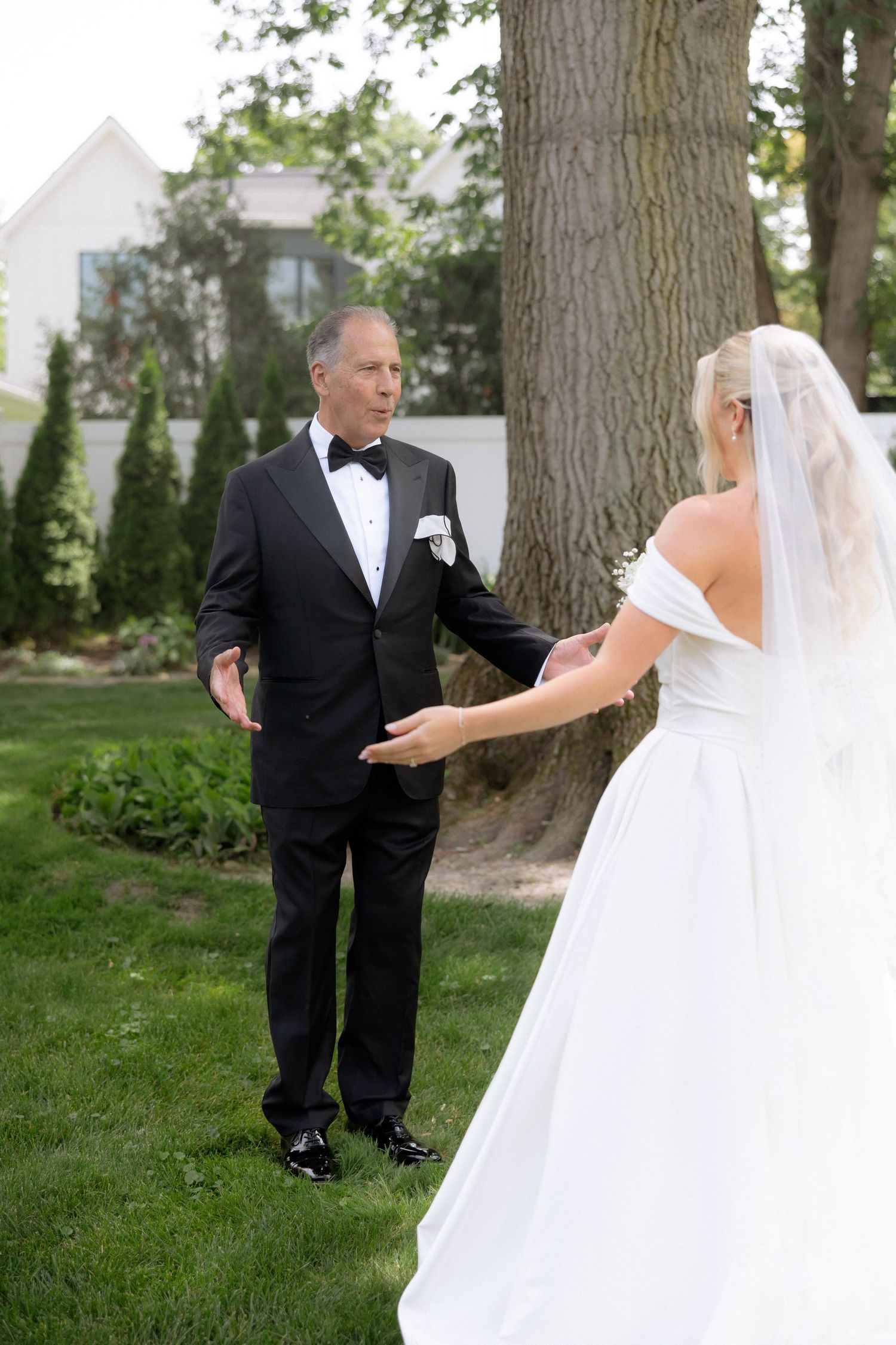 Emotional father-daughter first look moment as groom turns to see bride in white off-shoulder gown.