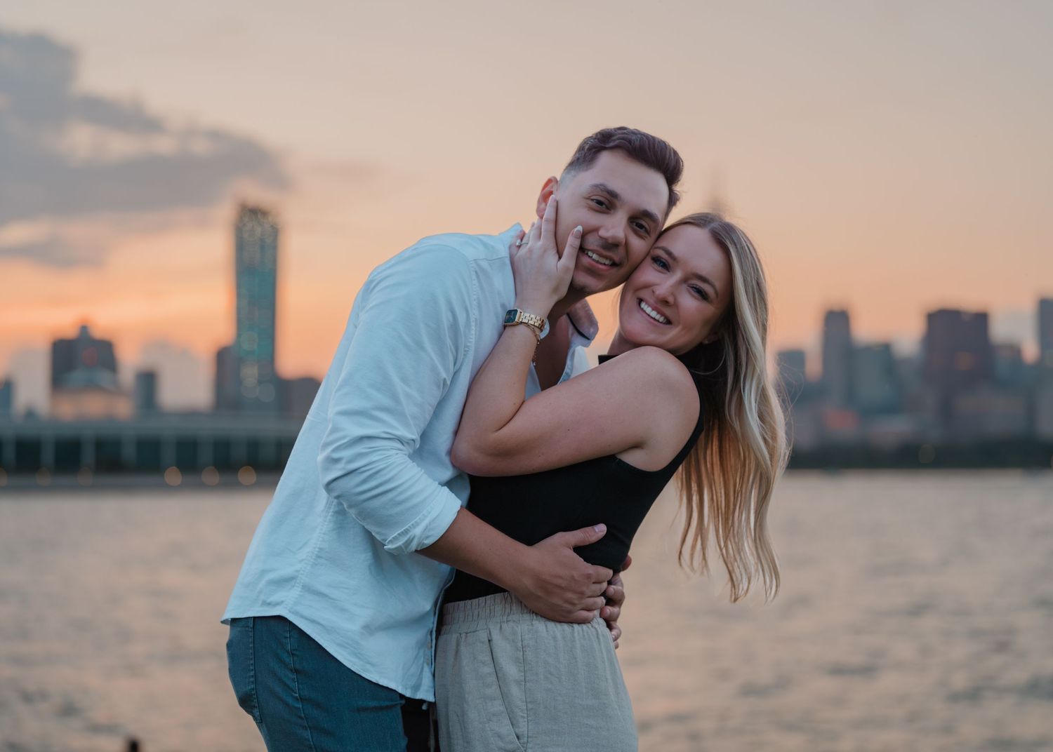 Joyful couple hugging and smiling together with a colorful city skyline at dusk.