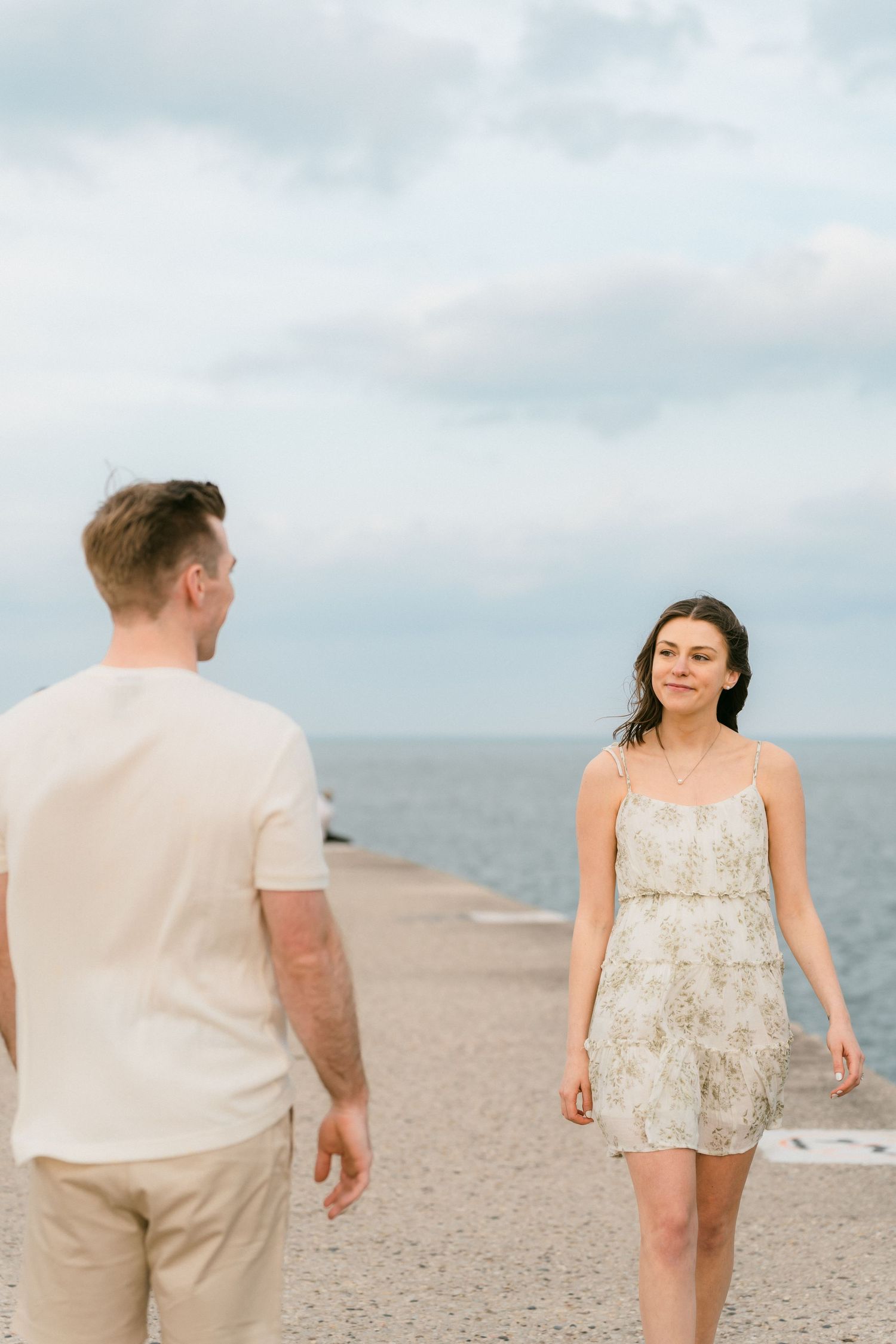 Couple walking toward each other on a lakeside pier under cloudy skies.