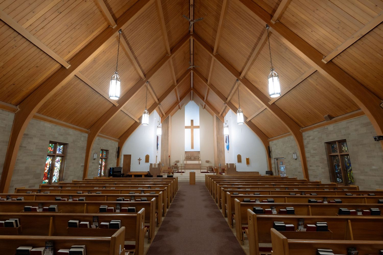 Serene church interior with wooden pews, vaulted ceiling, and a central cross above the altar bathed in natural light.