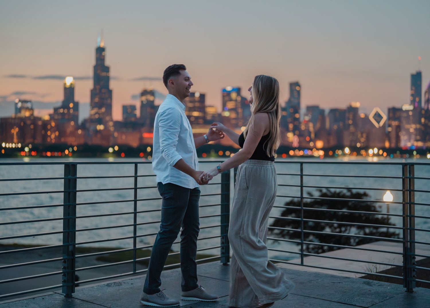 An engaged couple holds hands and shares a tender moment with the Chicago skyline at golden hour.