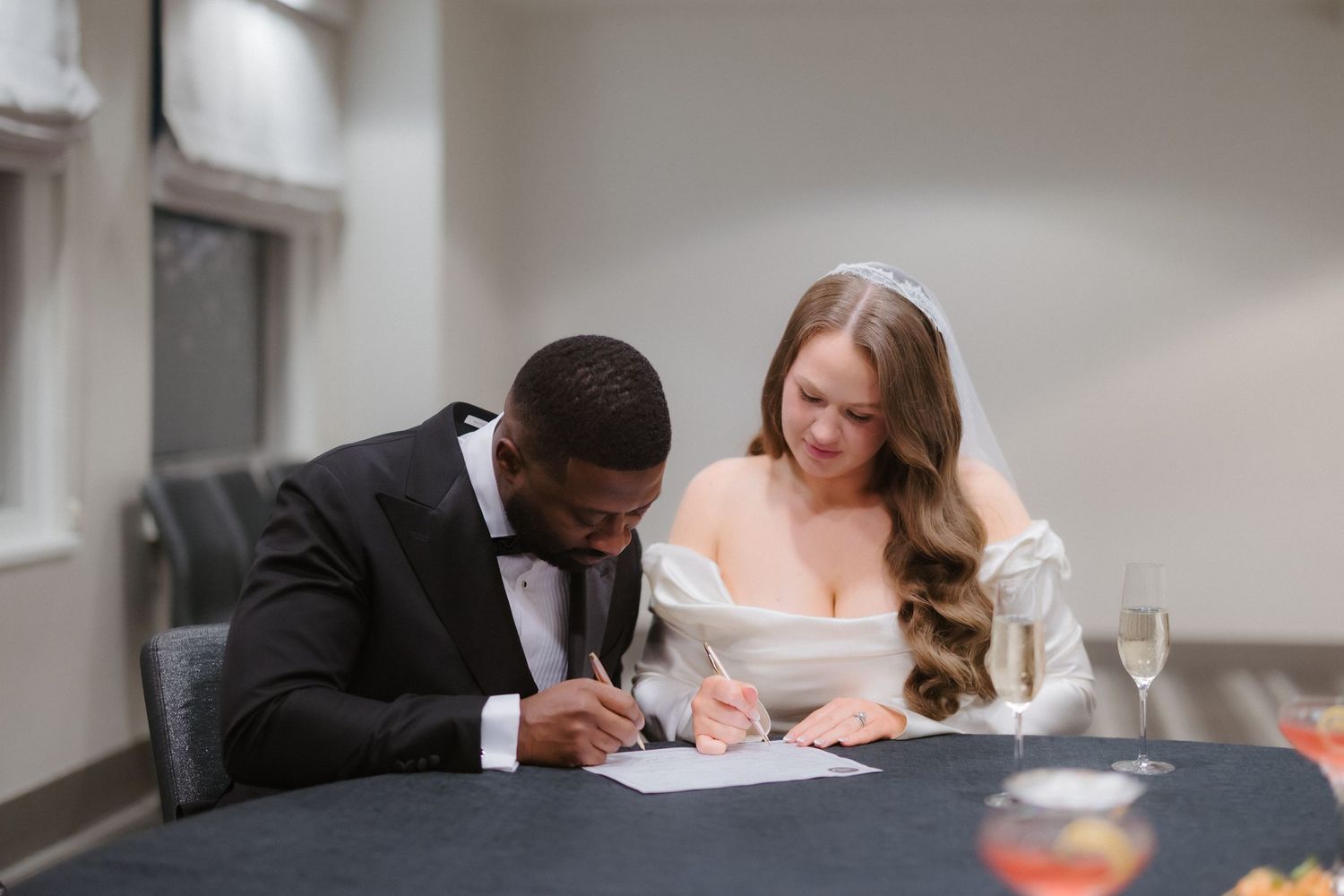 Bride and groom signing wedding documents at a table, dressed in elegant wedding attire.