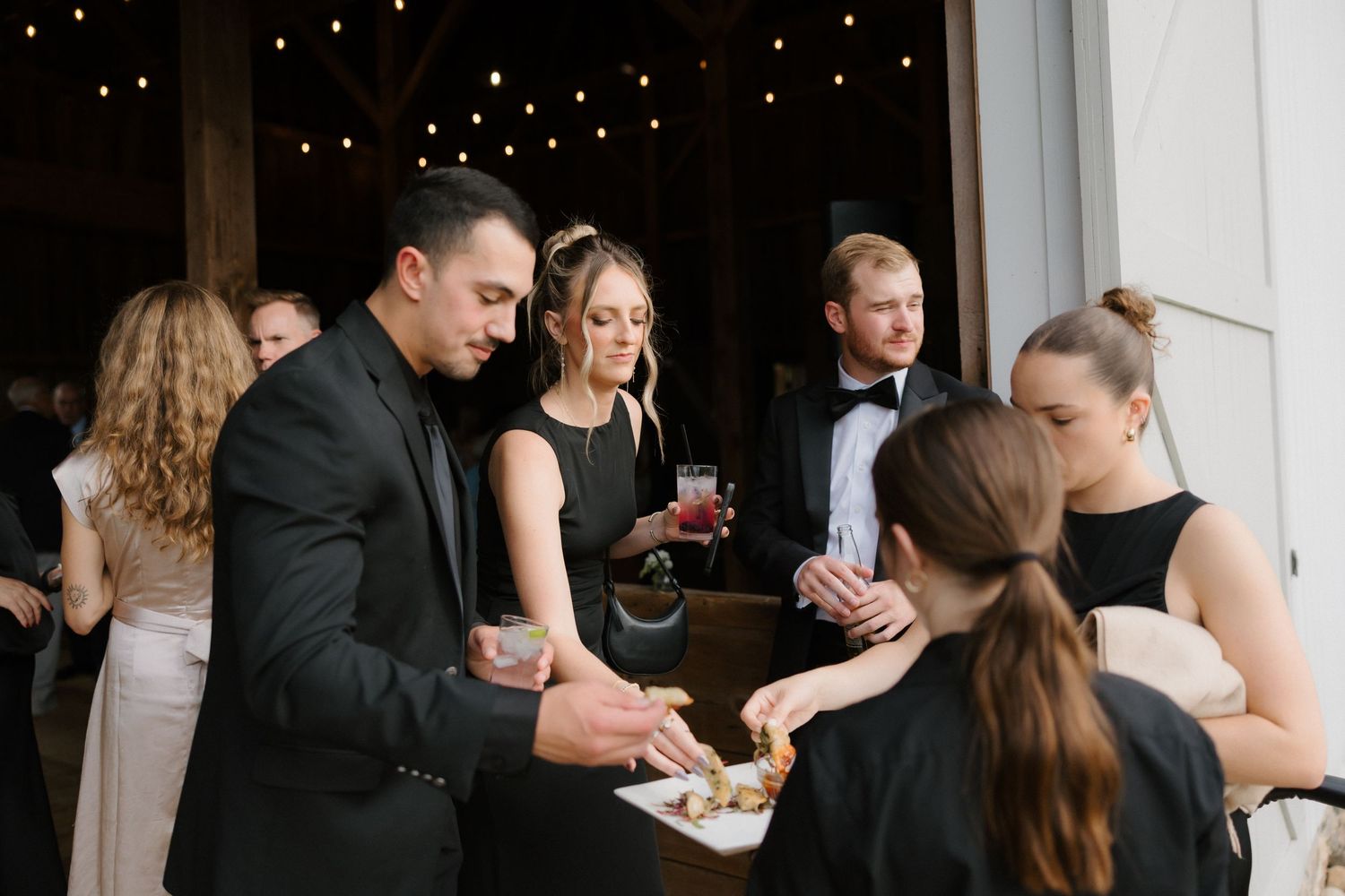 Wedding reception guests enjoying passed hors d oeuvres during cocktail hour under string lights.