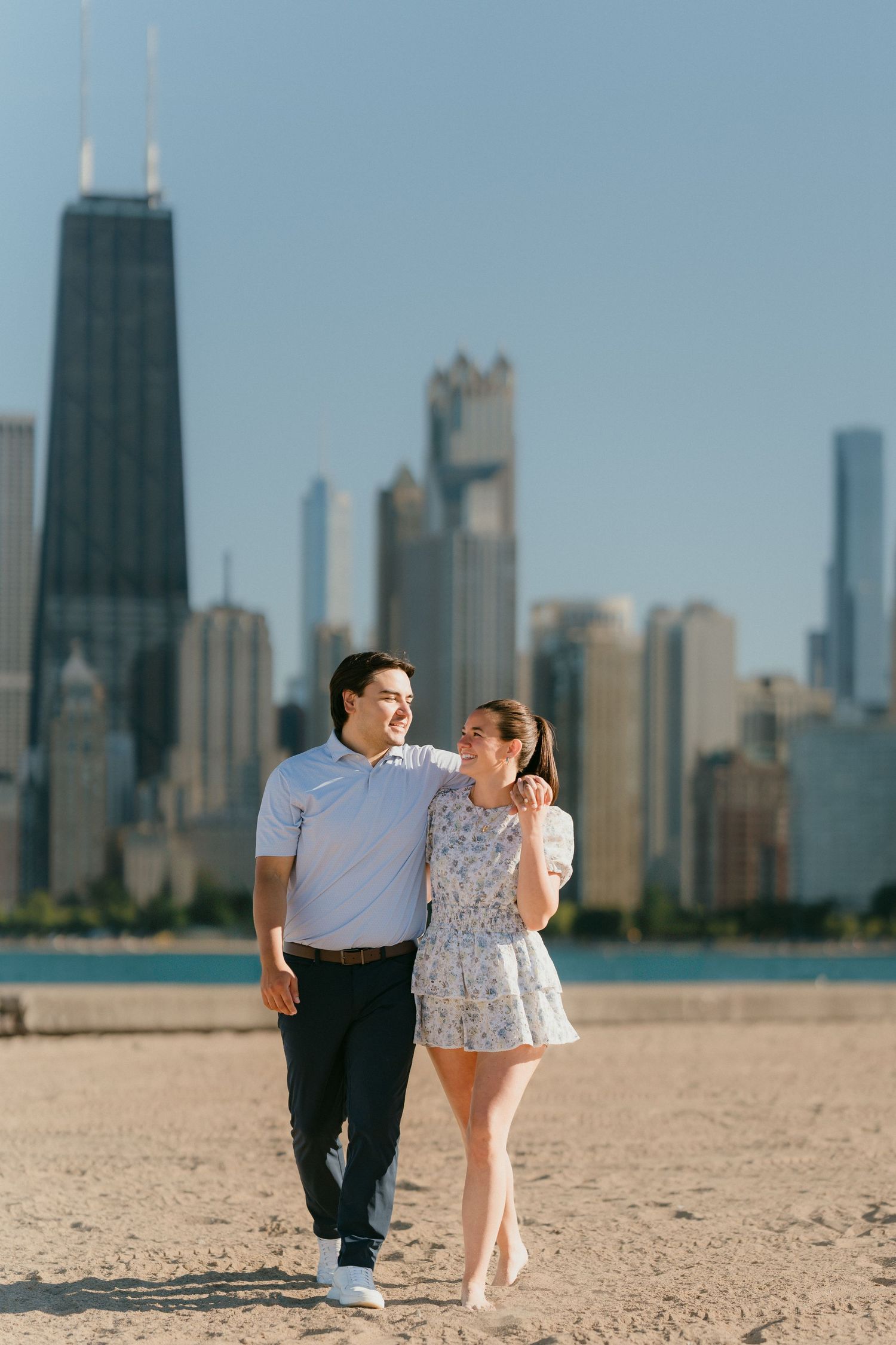 Happy couple walking on Chicago beach with iconic John Hancock Tower skyline backdrop.