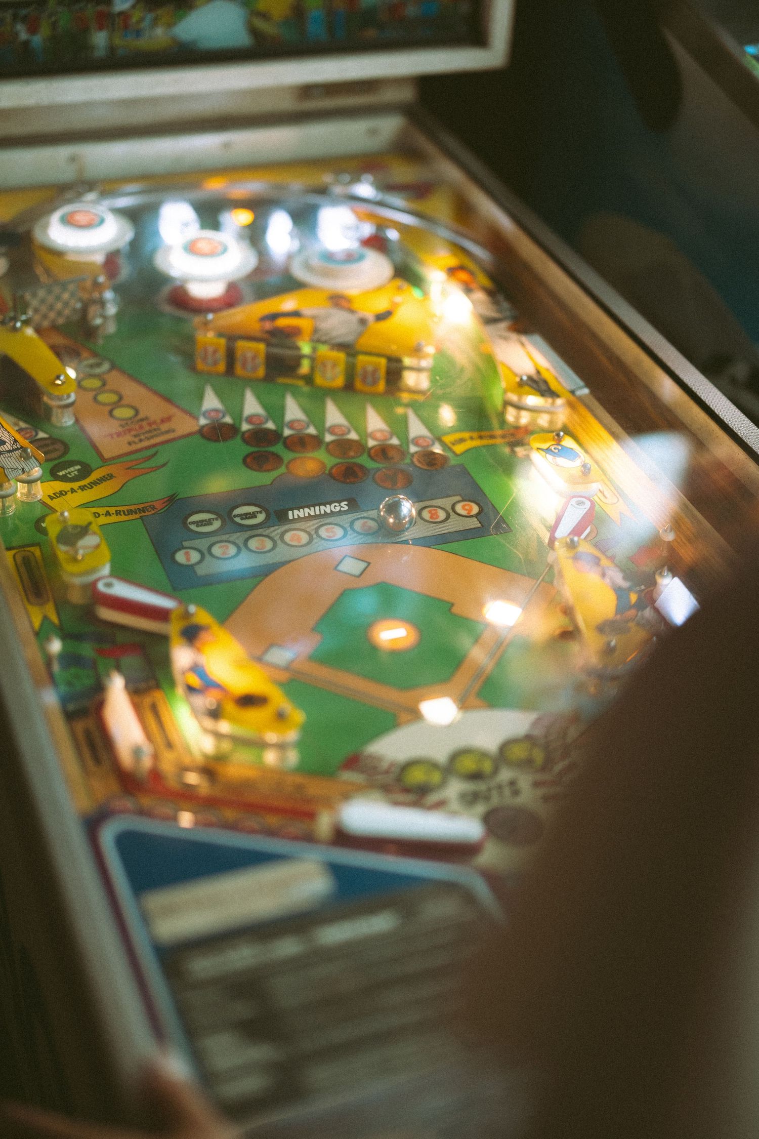 Illuminated baseball-themed pinball machine with colorful playfield and bumpers.