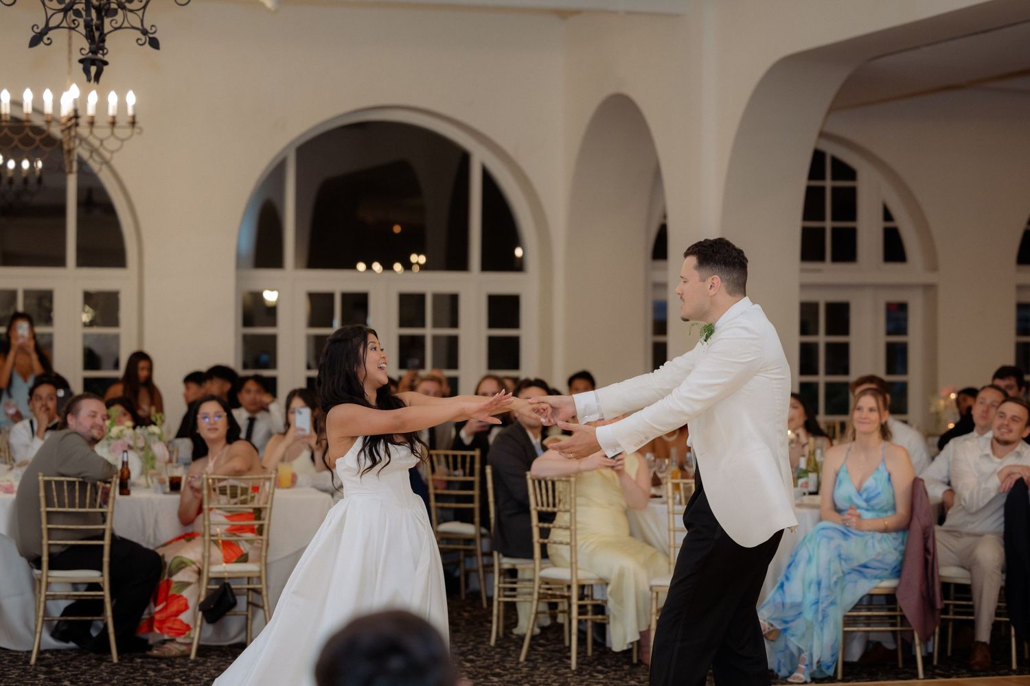 Bride and groom dancing together on wedding reception dance floor surrounded by seated guests.