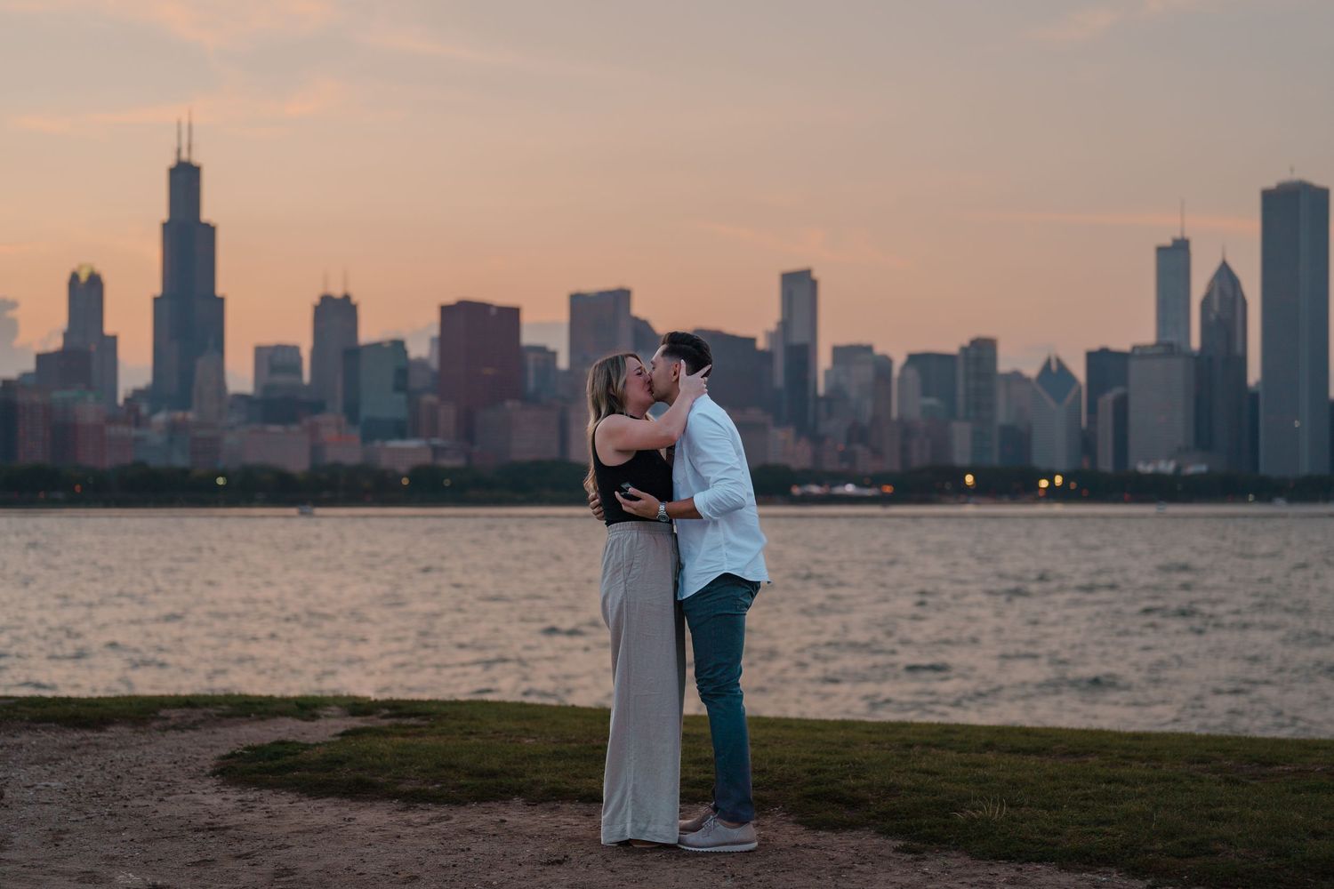 Couple sharing a romantic kiss at sunset with the Chicago skyline and Willis Tower reflected on Lake Michigan.
