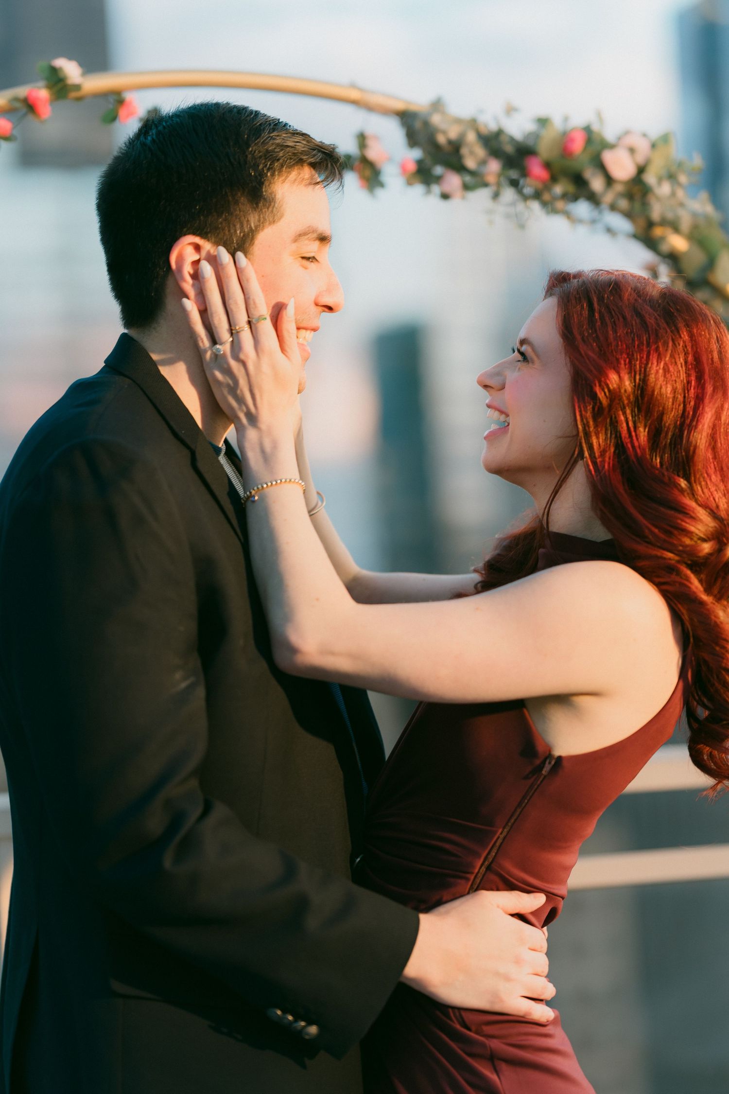Joyful woman with red hair cradles mans face after Chicago rooftop proposal at golden hour.