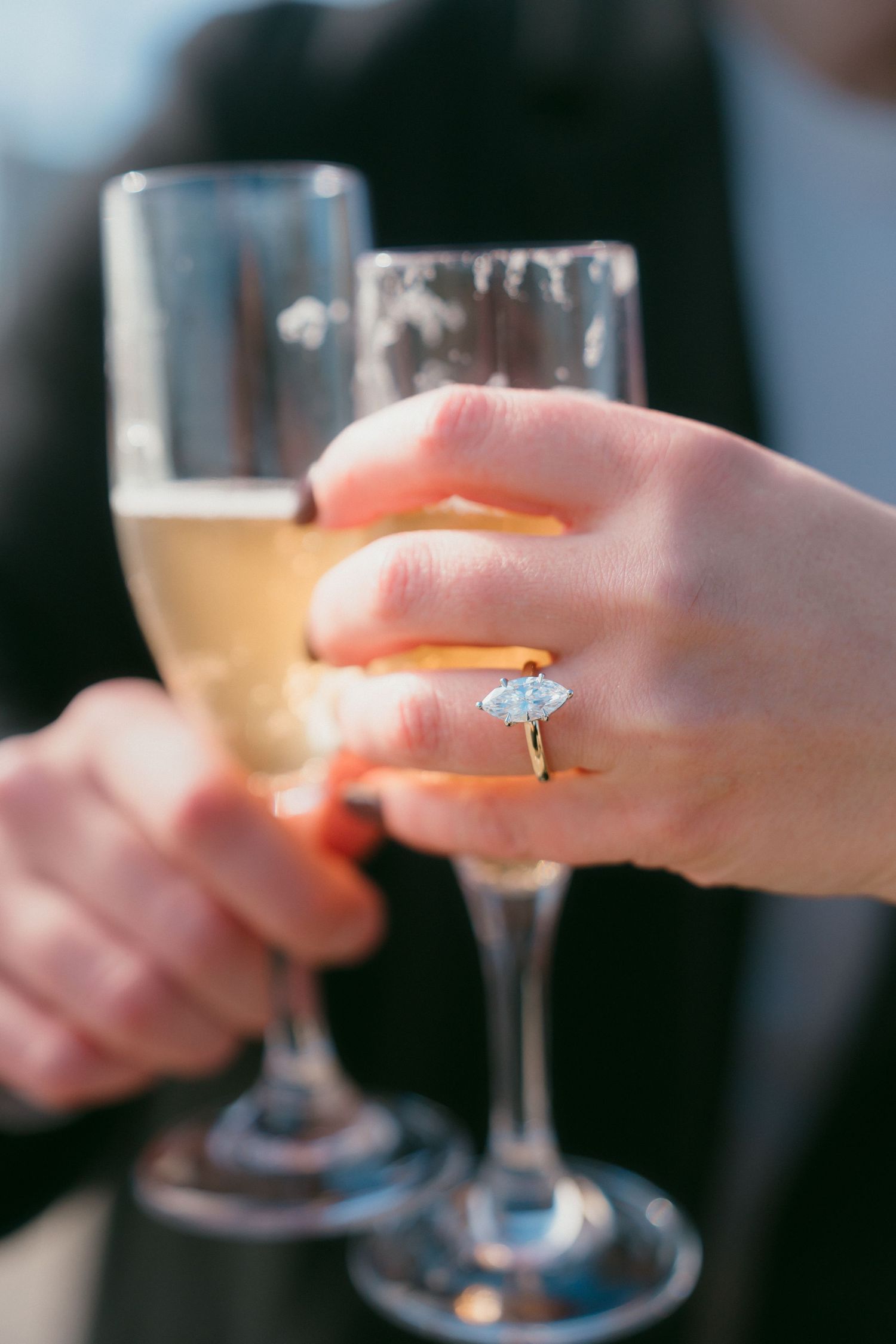 Close-up of an engagement ring on a hand holding a champagne flute during a celebration.