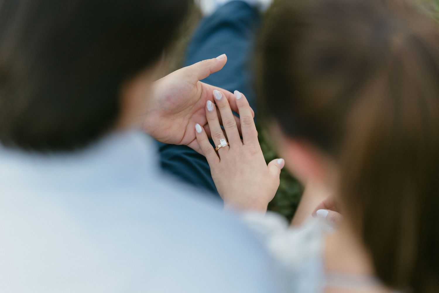 Close-up of woman's hand showing diamond engagement ring resting on partner's arm during outdoor photo session.