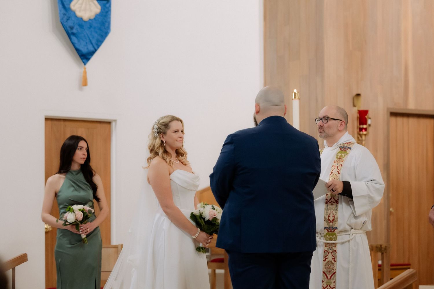 Bride and groom holding hands at church altar with bridesmaid and officiant during intimate wedding ceremony.