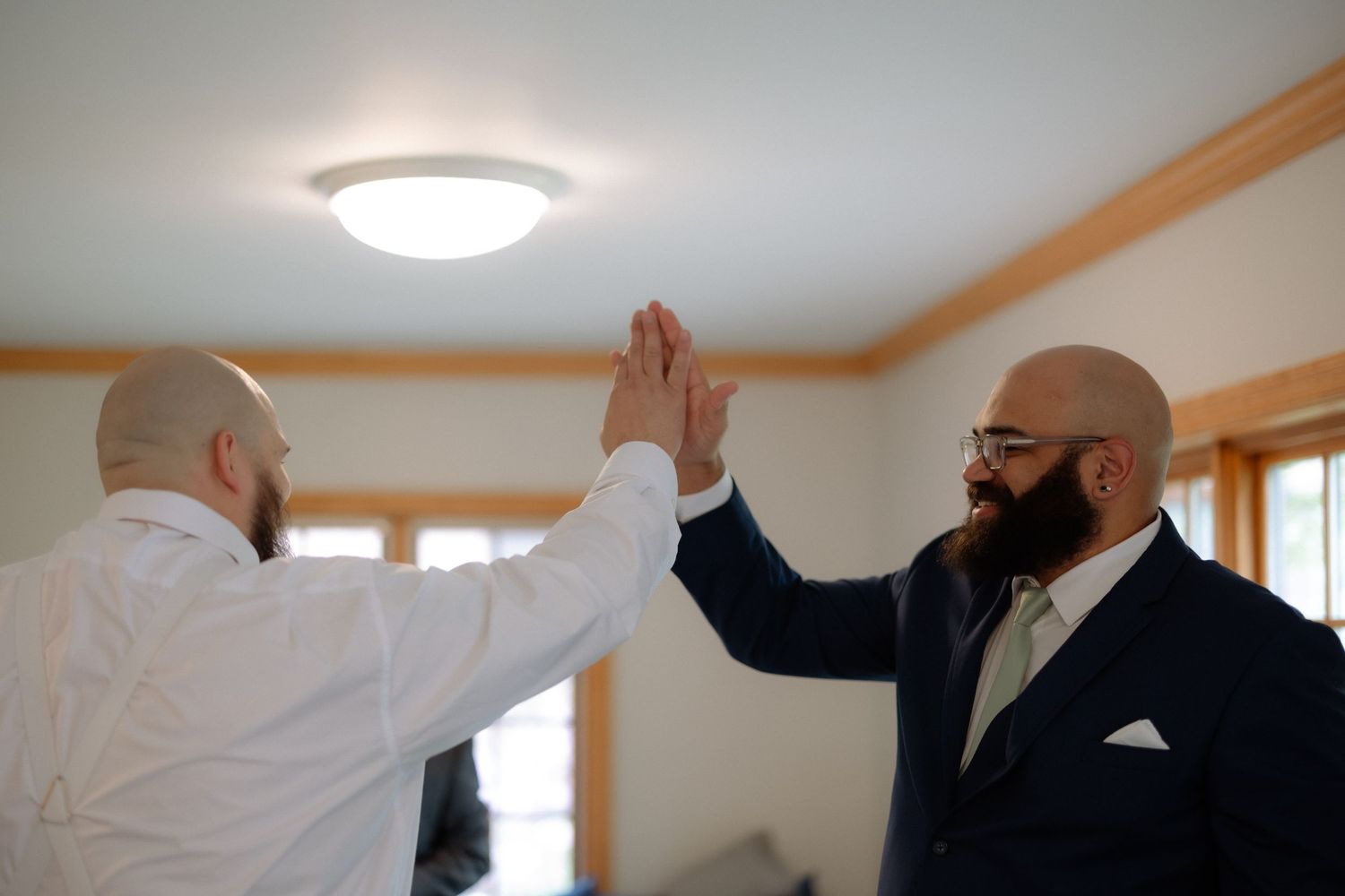 Two bald men in formal attire giving a high five indoors, celebrating a special occasion.