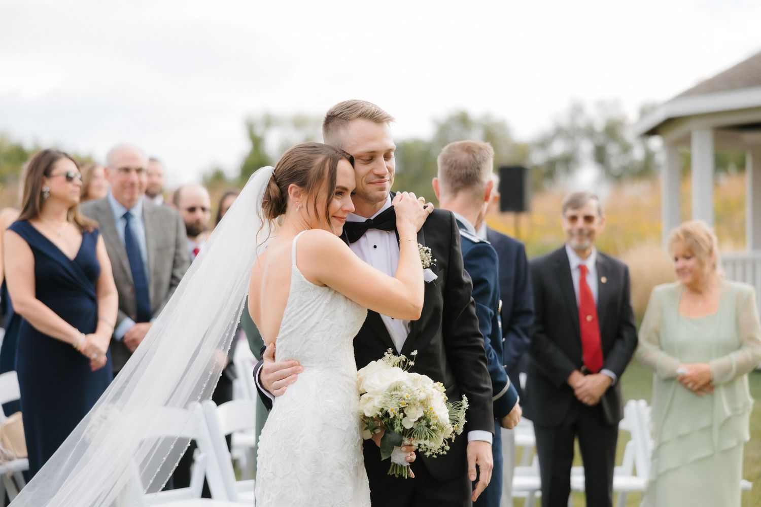 Bride and groom share emotional embrace while walking back up the aisle after outdoor wedding ceremony.
