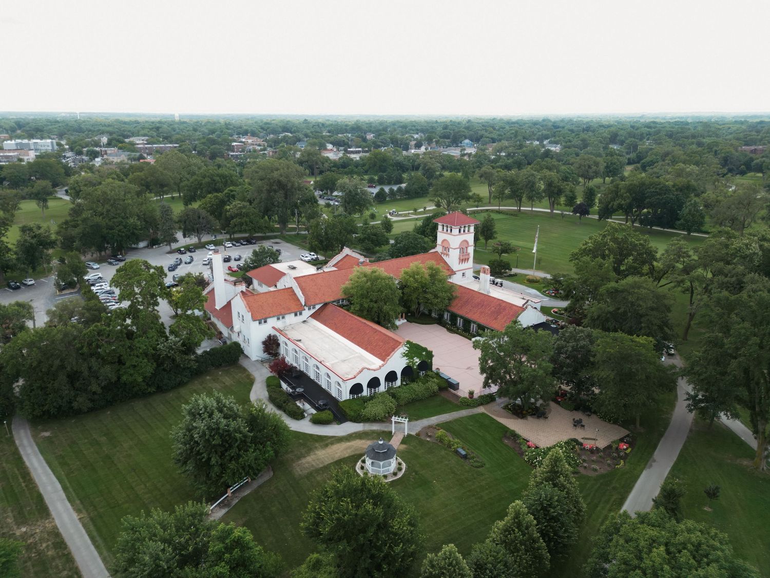 Aerial view of a large Spanish-style estate with red tile roofs surrounded by lush green trees and manicured grounds.