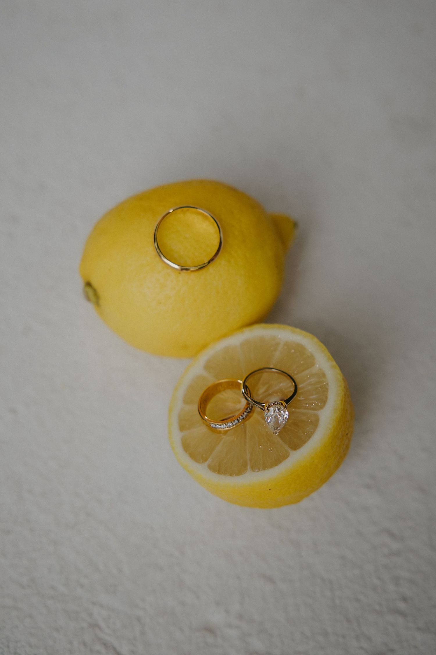 Gold wedding rings resting on a fresh cut lemon half beside a whole lemon on white surface.