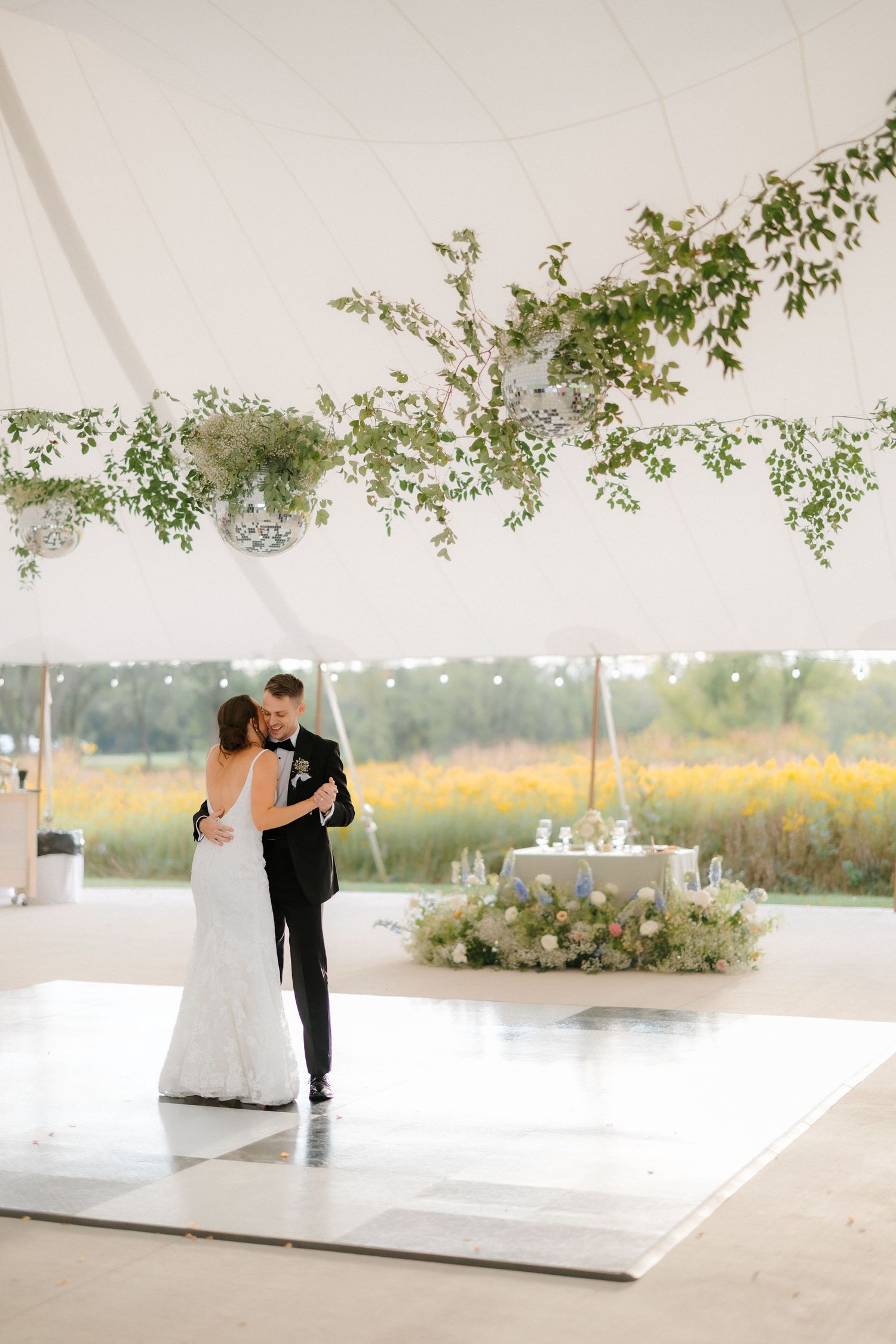 Bride and groom share intimate first dance under a elegant tent adorned with greenery and disco balls at their wedding.