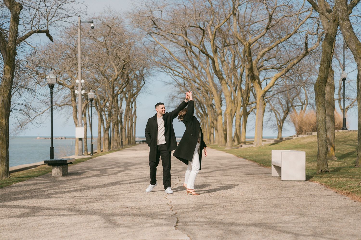 Couple dancing on a tree-lined park path near the waterfront in early spring.
