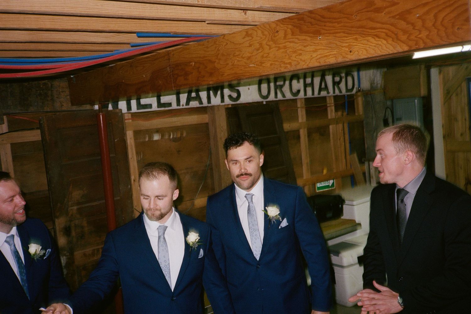 Groomsmen in navy blue suits with boutonnieres stand together at Williams Orchard wedding venue.