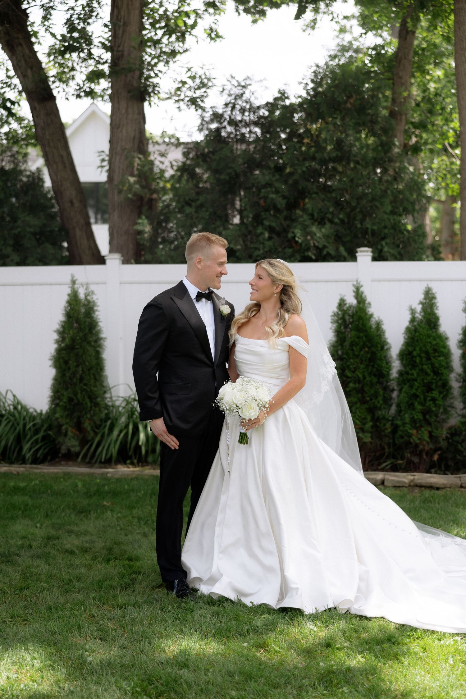 Bride and groom share a romantic moment in a garden, bride holding a white floral bouquet.