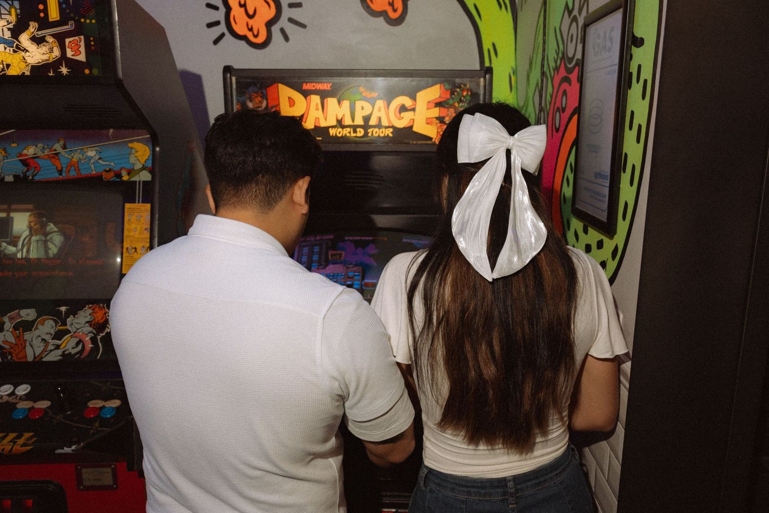 A couple plays the Rampage World Tour arcade game together at a retro gaming arcade.
