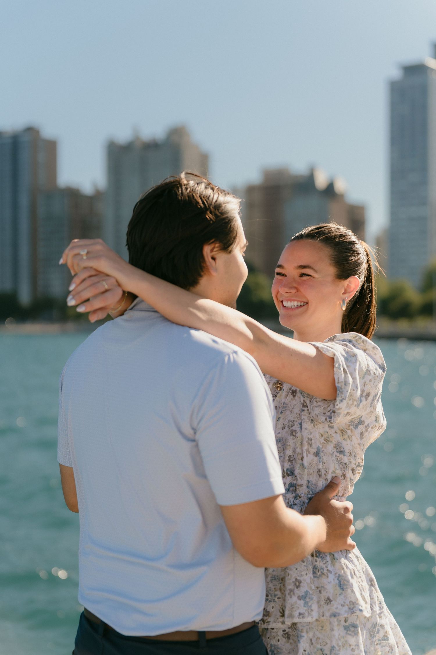 Smiling couple embracing near Lake Michigan with Chicago skyline in background on sunny day.