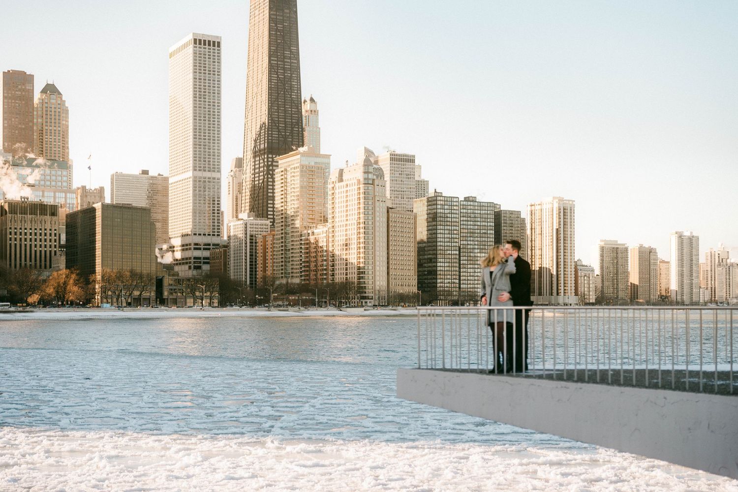 Couple embracing on snowy Chicago lakefront pier with stunning city skyline view.