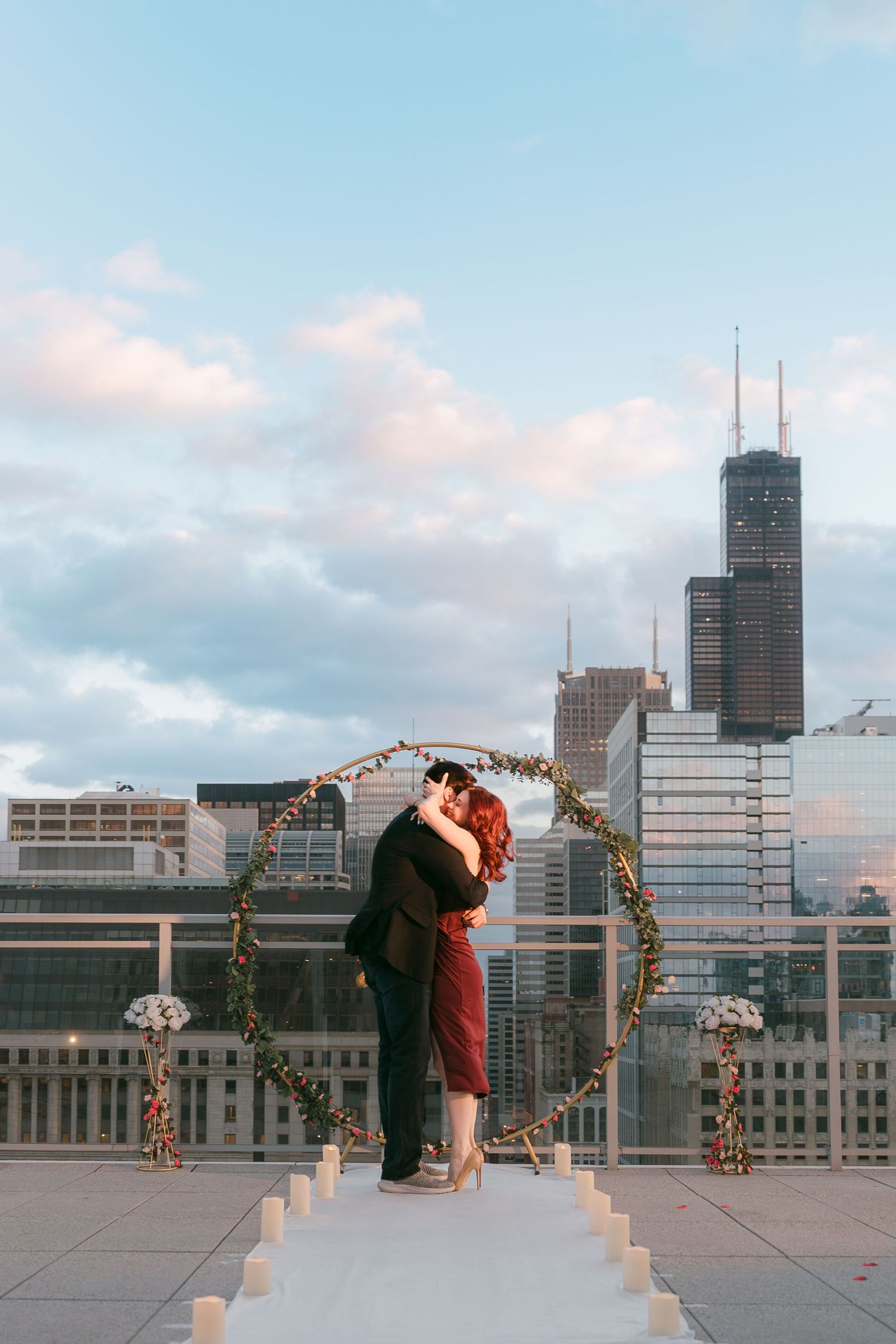 Couple sharing a romantic kiss under a circular floral arch on a rooftop with Chicago skyline.
