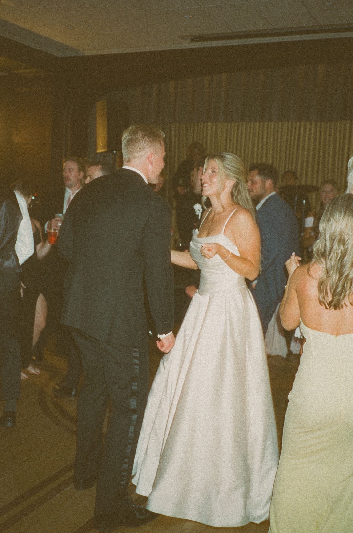 Bride and groom dancing together at wedding reception, bride in elegant white ball gown holding hands with groom.