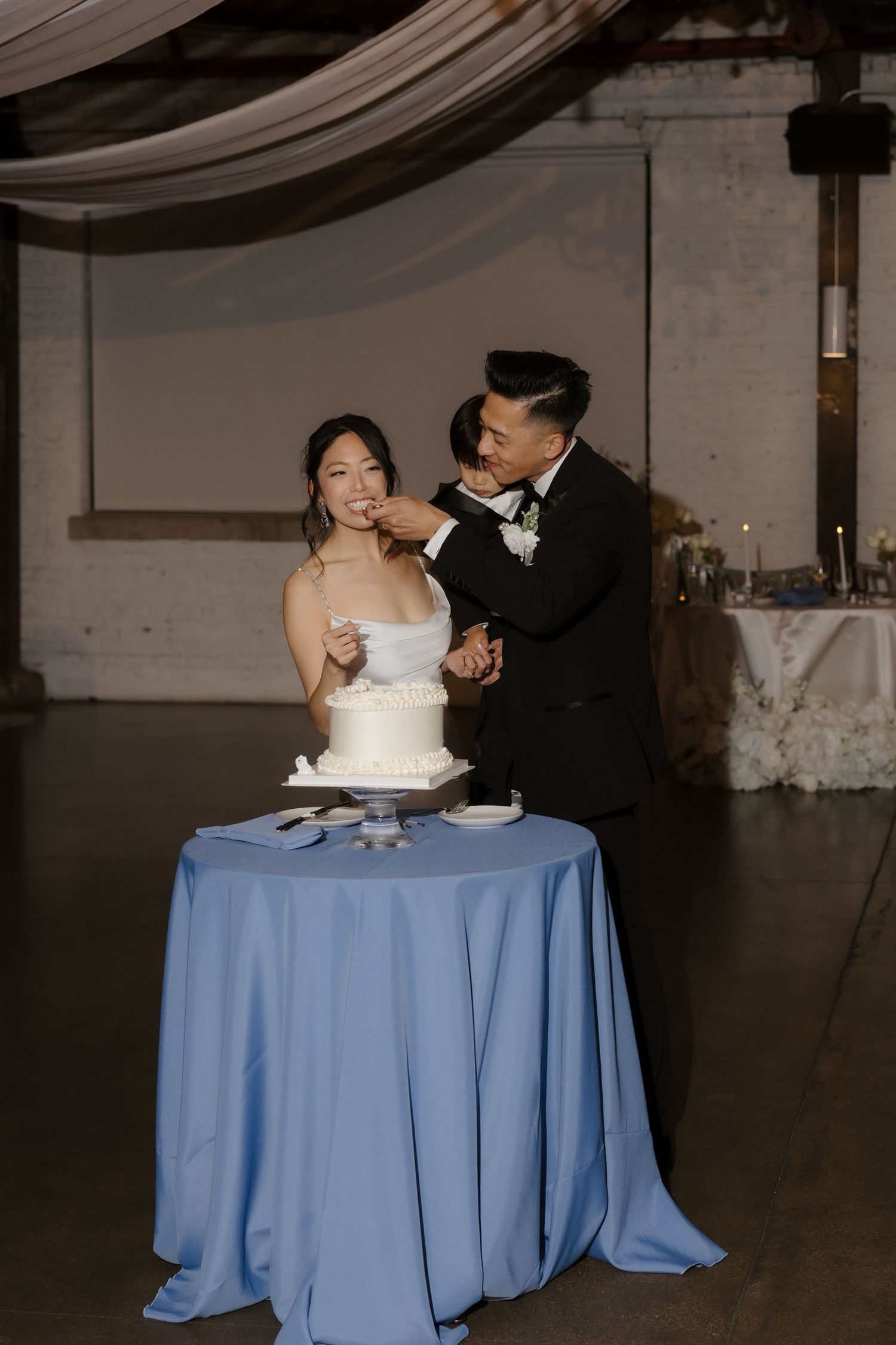 Groom feeds bride a bite of white wedding cake at reception.