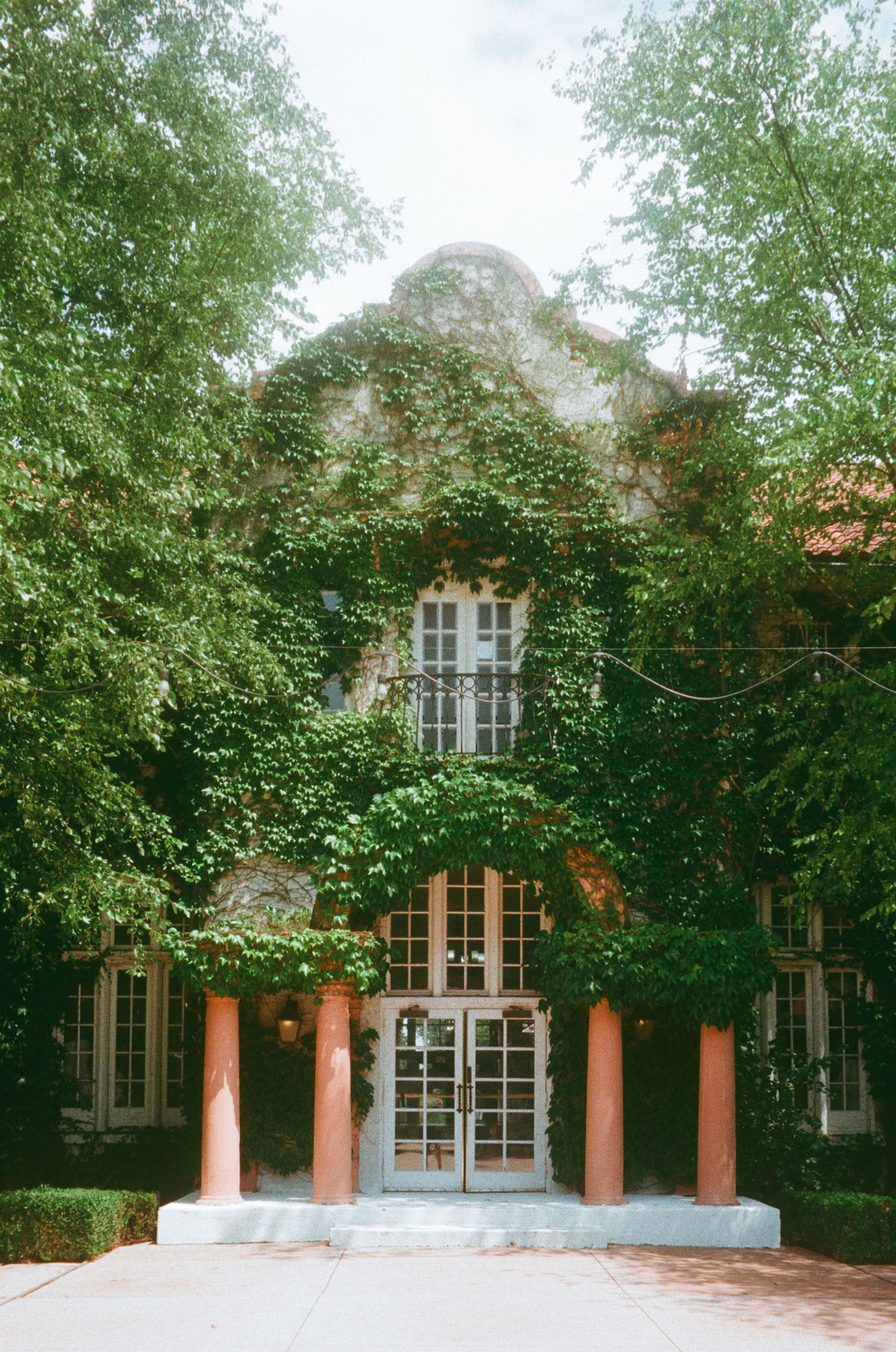 Ivy-covered historic building with coral columns and French doors surrounded by lush green trees.