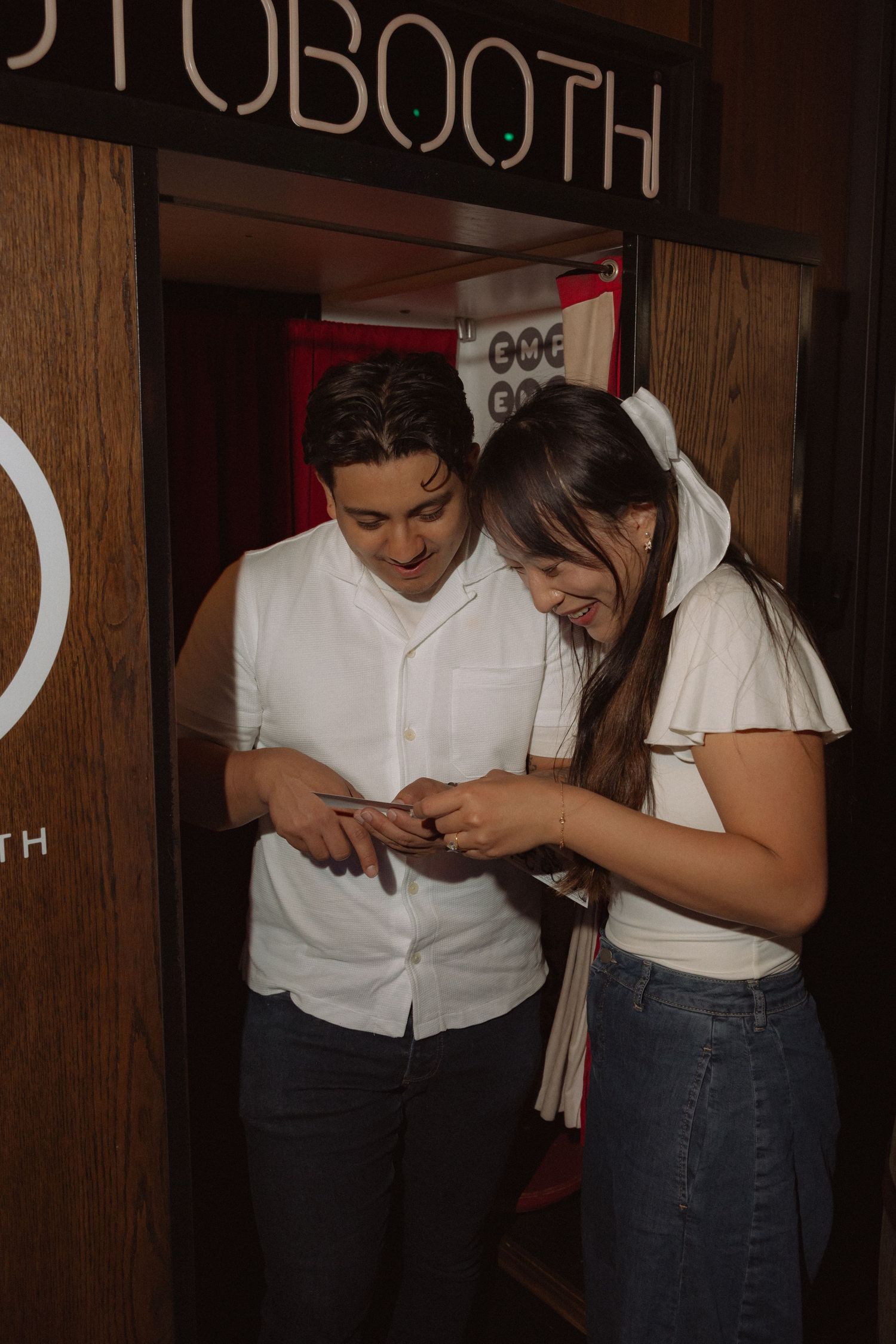 Couple smiling and looking at a phone together outside a photo booth entrance.