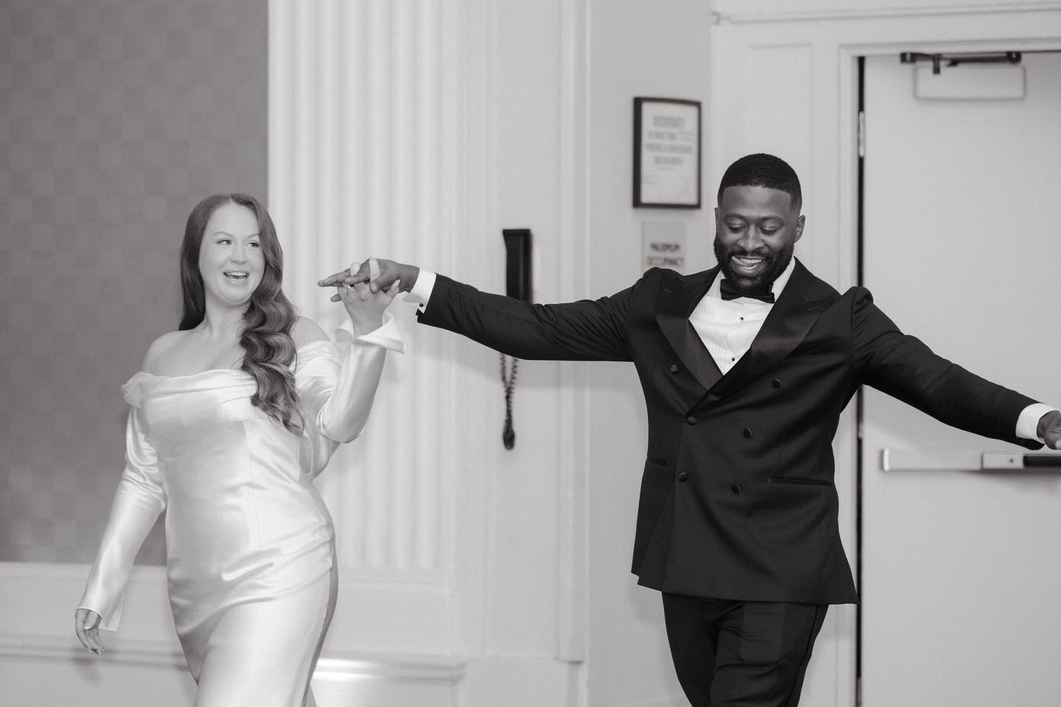 Black and white photo of a bride and groom dancing joyfully at their wedding reception.