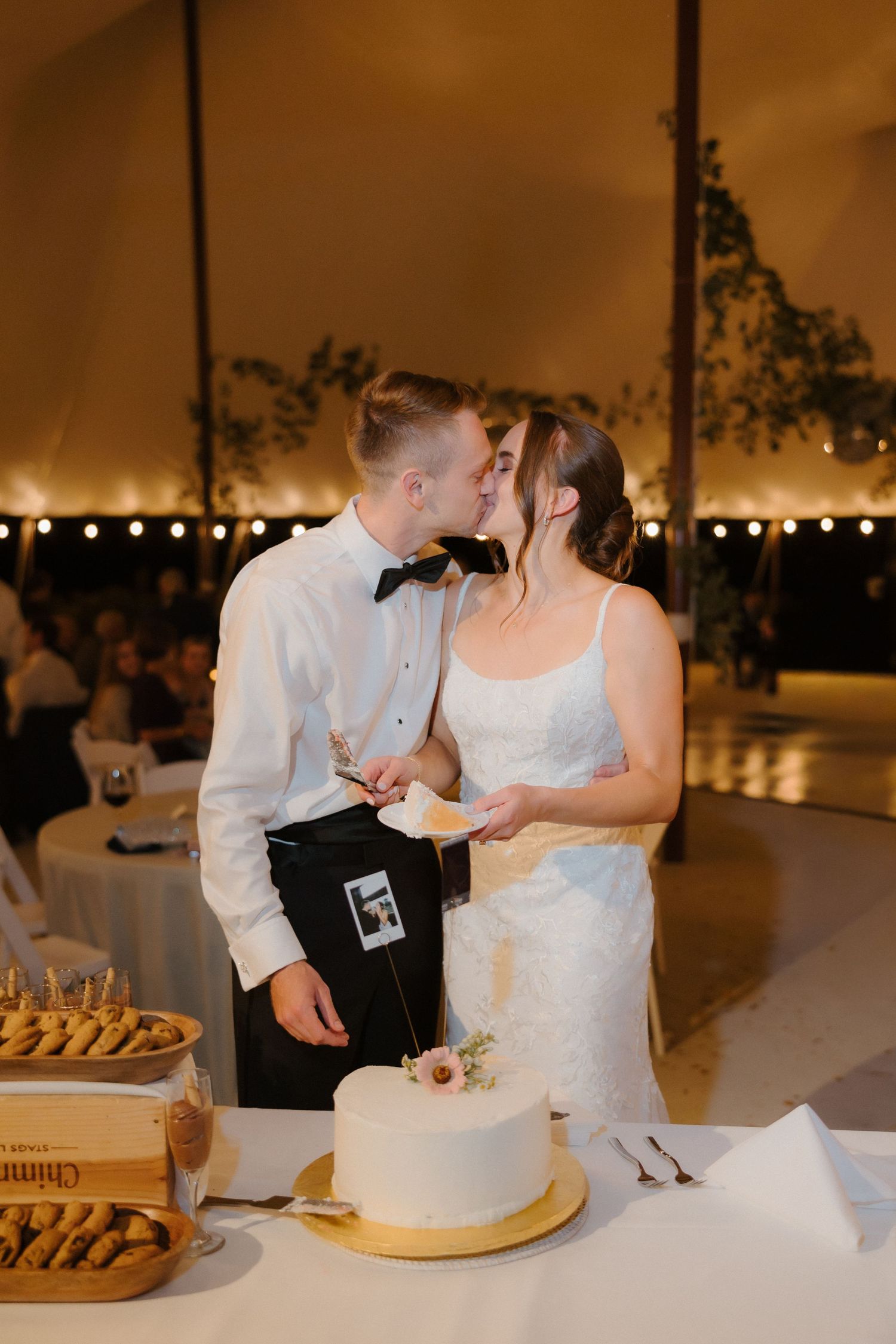 Newlyweds share a sweet kiss after cutting their white wedding cake at their elegant reception.
