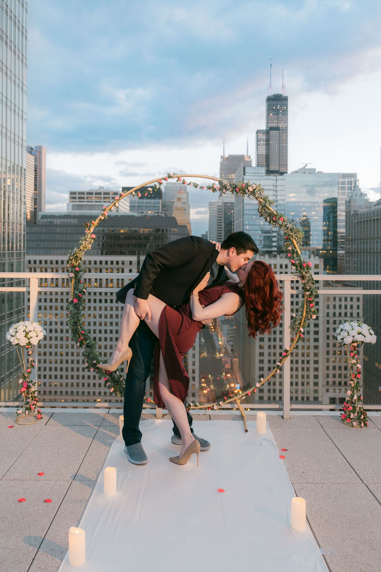 Couple sharing romantic dip kiss in front of lit floral arch on Chicago rooftop.