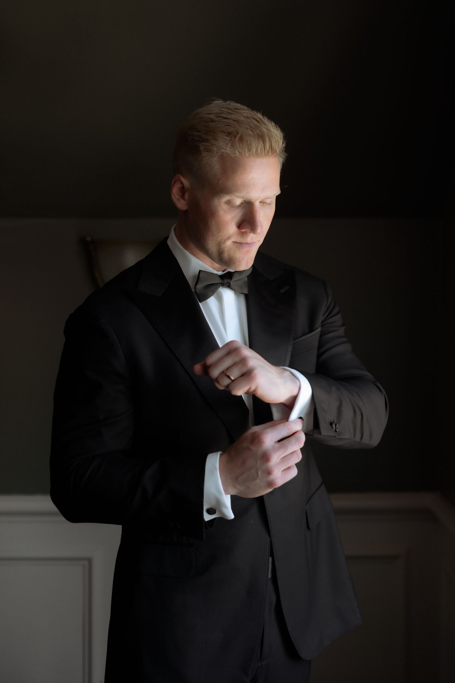 Groom in black tuxedo adjusting cufflinks while getting ready for wedding.