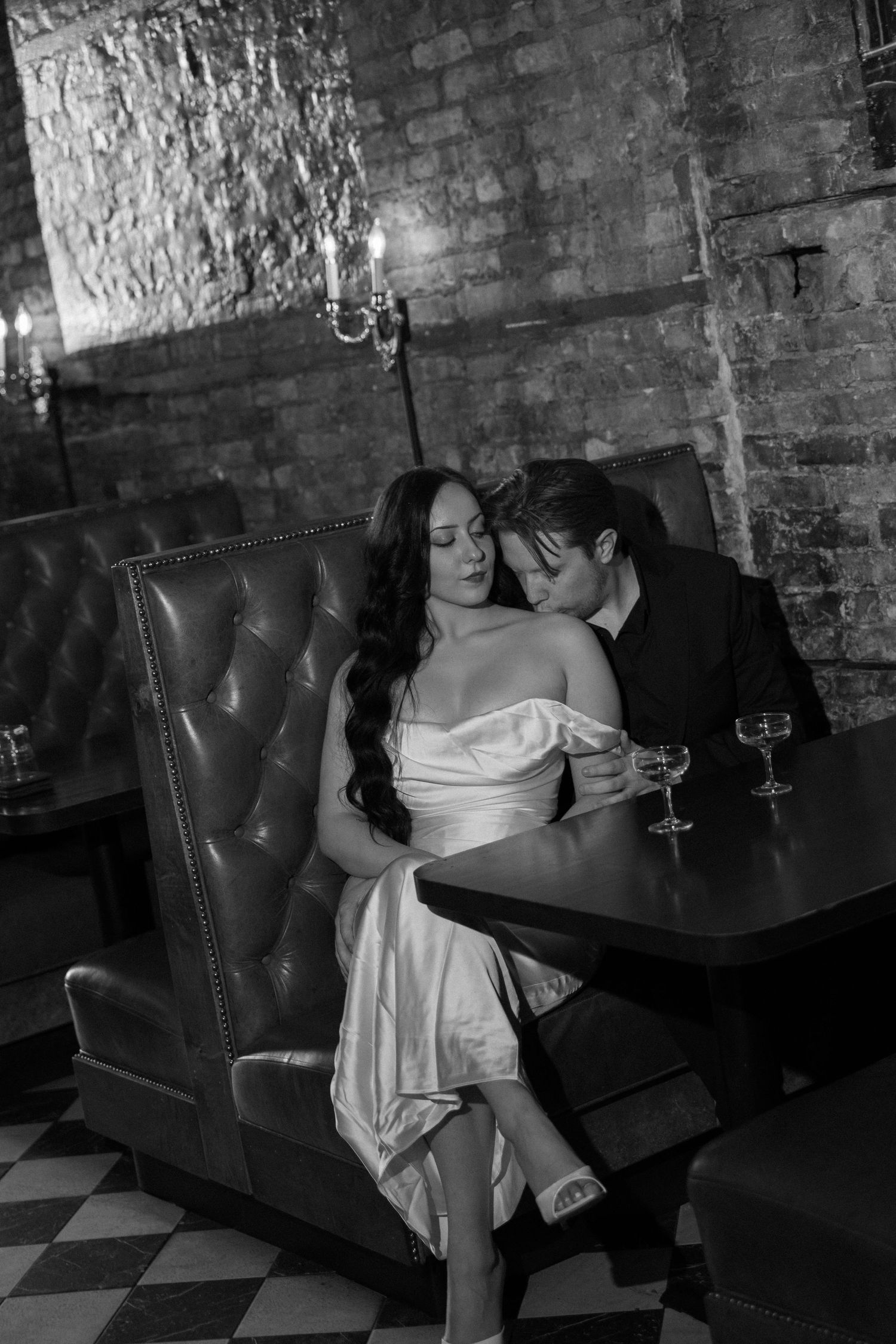 Black and white photo of a bride and groom sharing an intimate moment in a leather booth at an upscale restaurant.