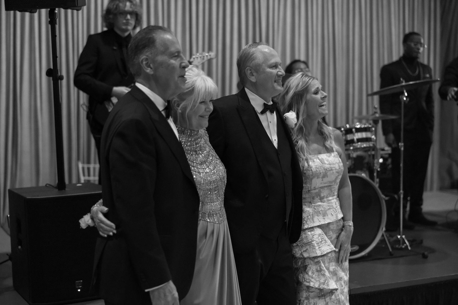 Two couples in formal attire posing together at wedding reception in black and white photo.