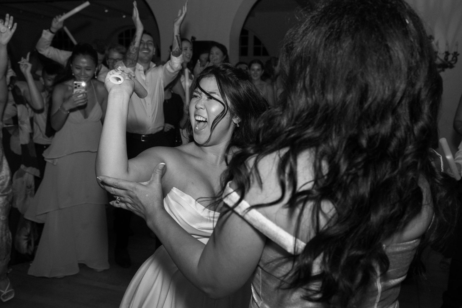 Bridesmaid laughs with joy while dancing with another guest at a lively black and white wedding reception.