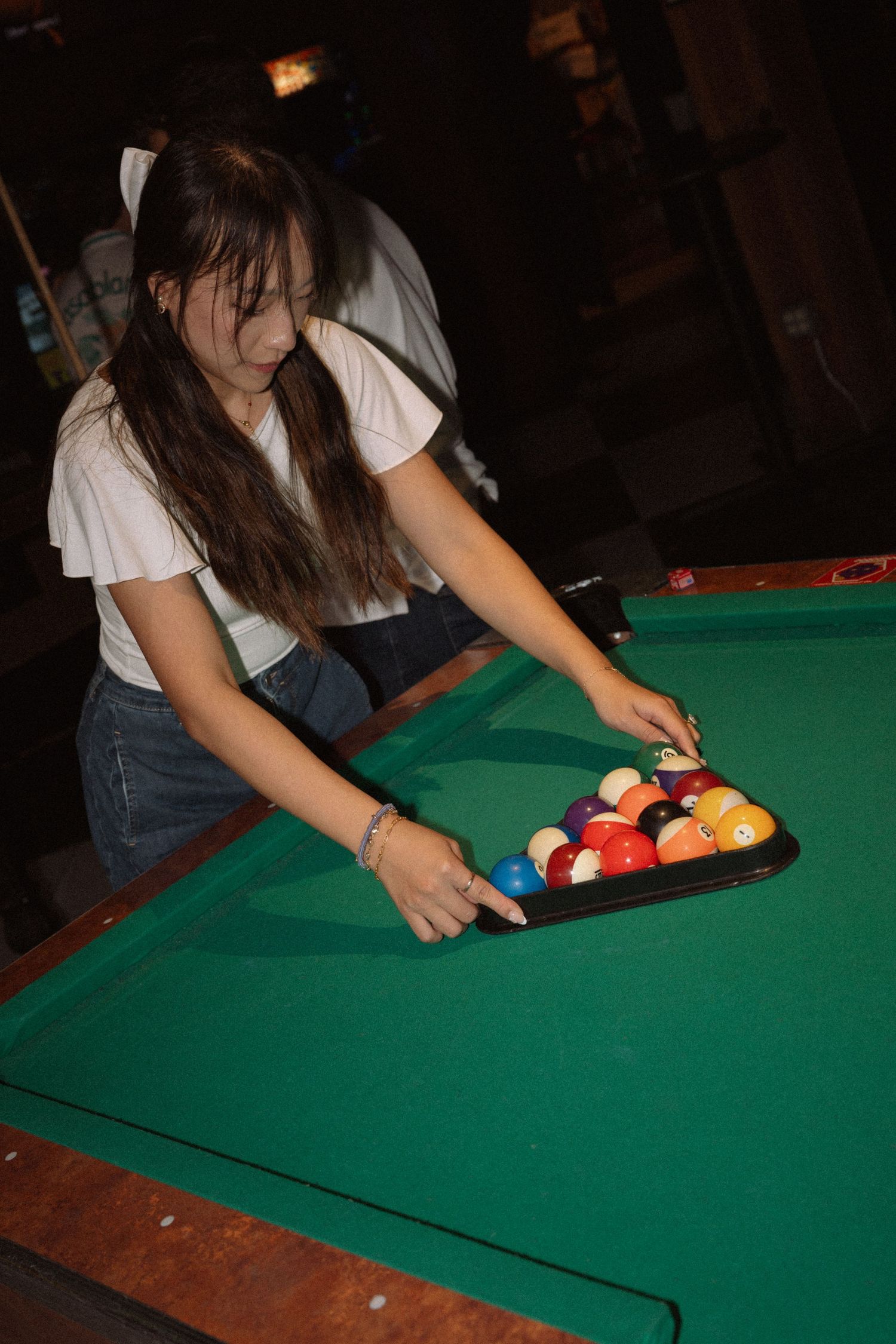 Young woman setting up billiard balls in a triangle rack on a green pool table in a bar.
