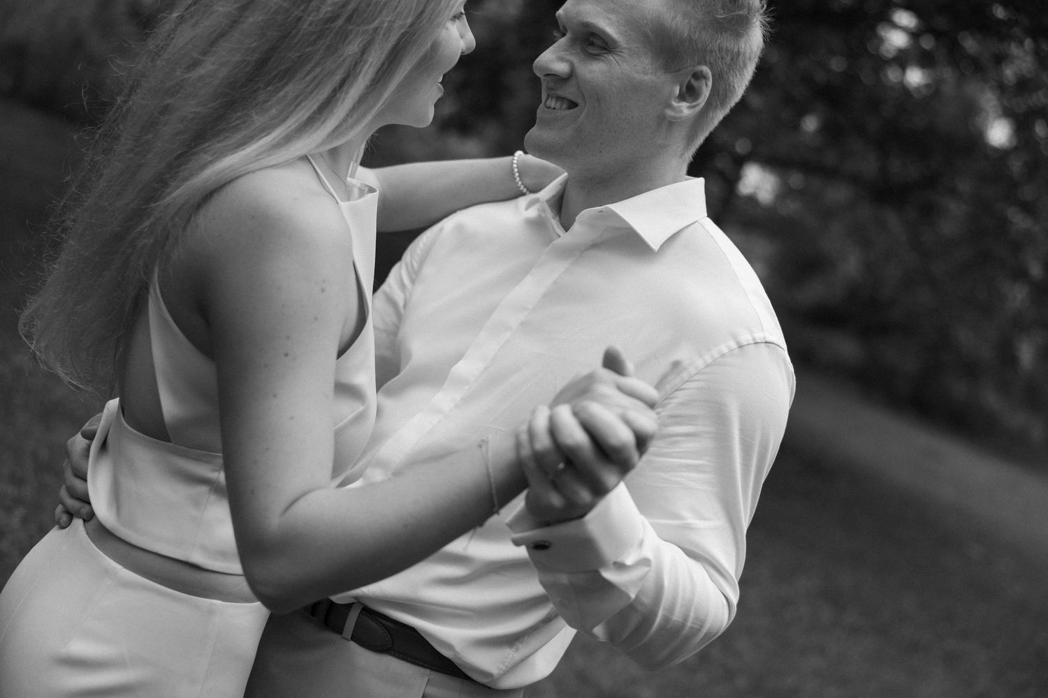 Black and white photo of a couple dancing outdoors, smiling and holding hands in a romantic embrace.
