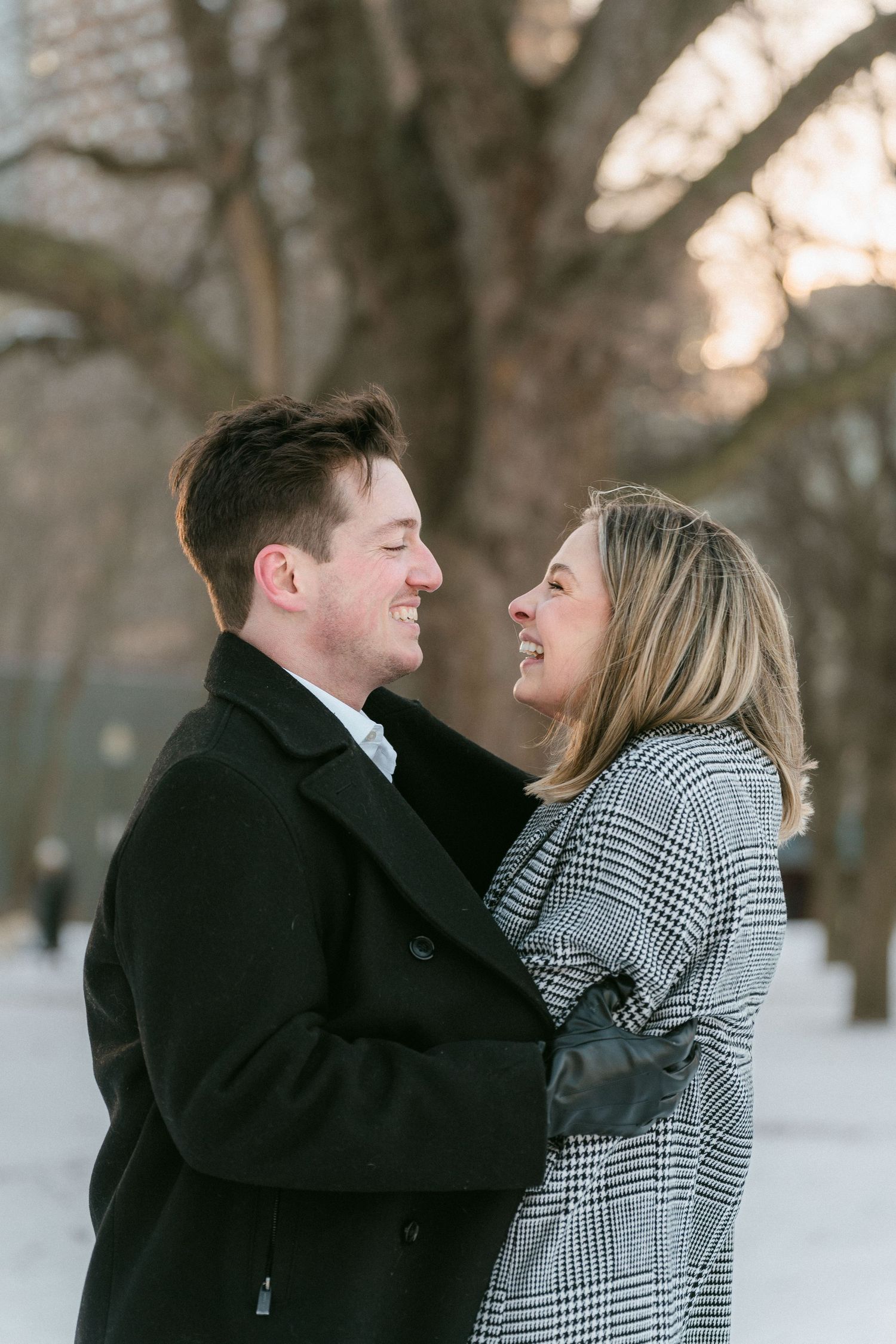 Happy couple smiling and embracing outdoors in winter, dressed in black and grey plaid coats with snow background.