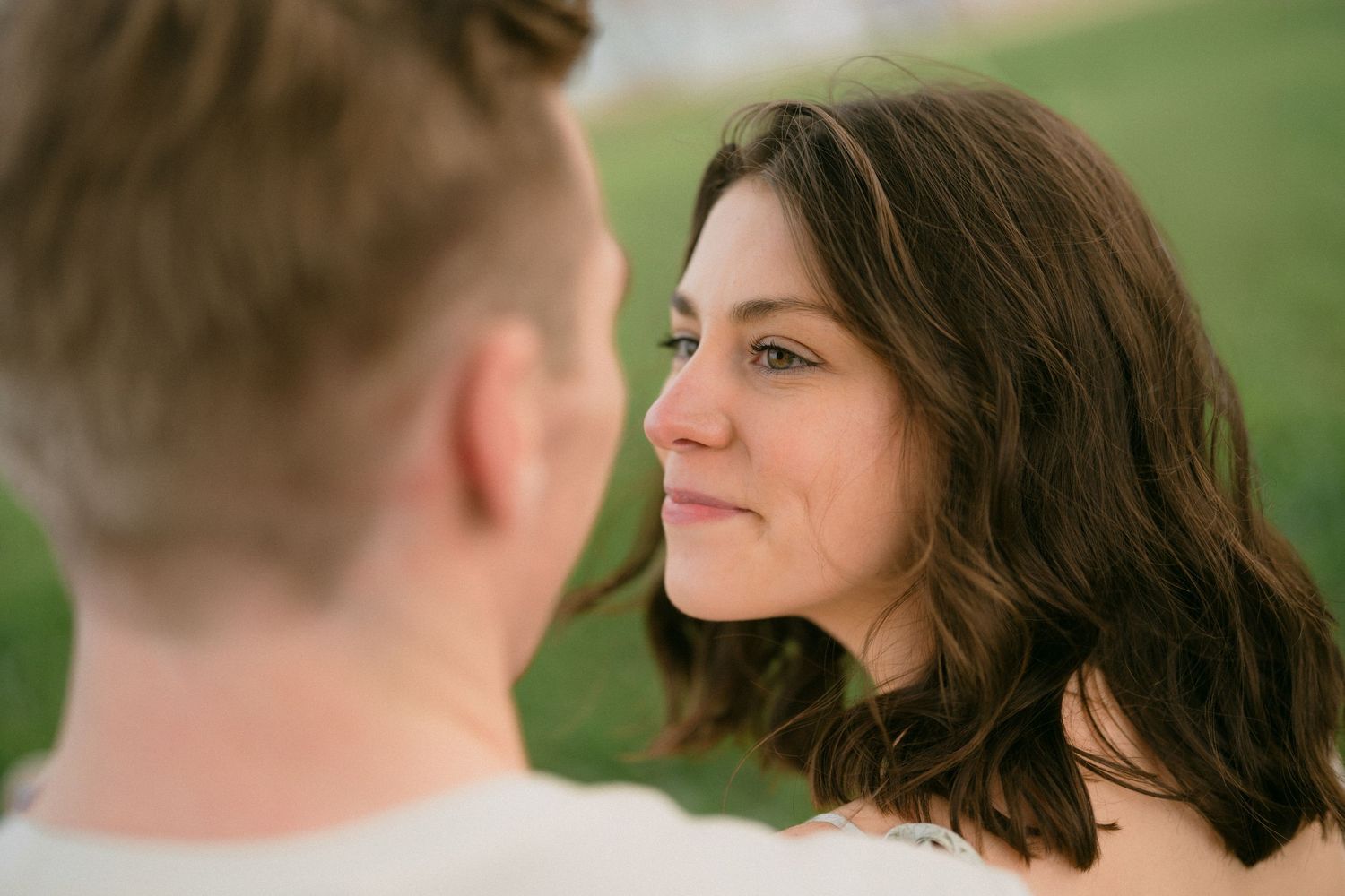 A brunette woman gazes lovingly at her partner in a soft outdoor portrait.