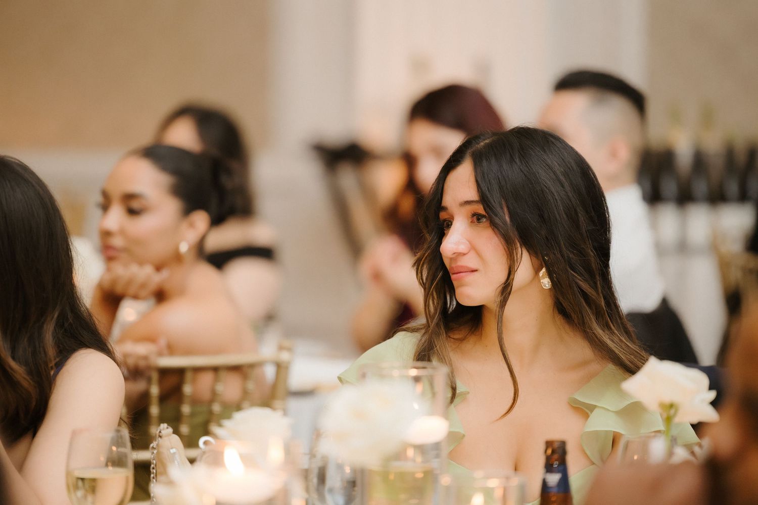Elegant woman with dark hair smiling at a wedding reception dinner table with candles and white flowers.